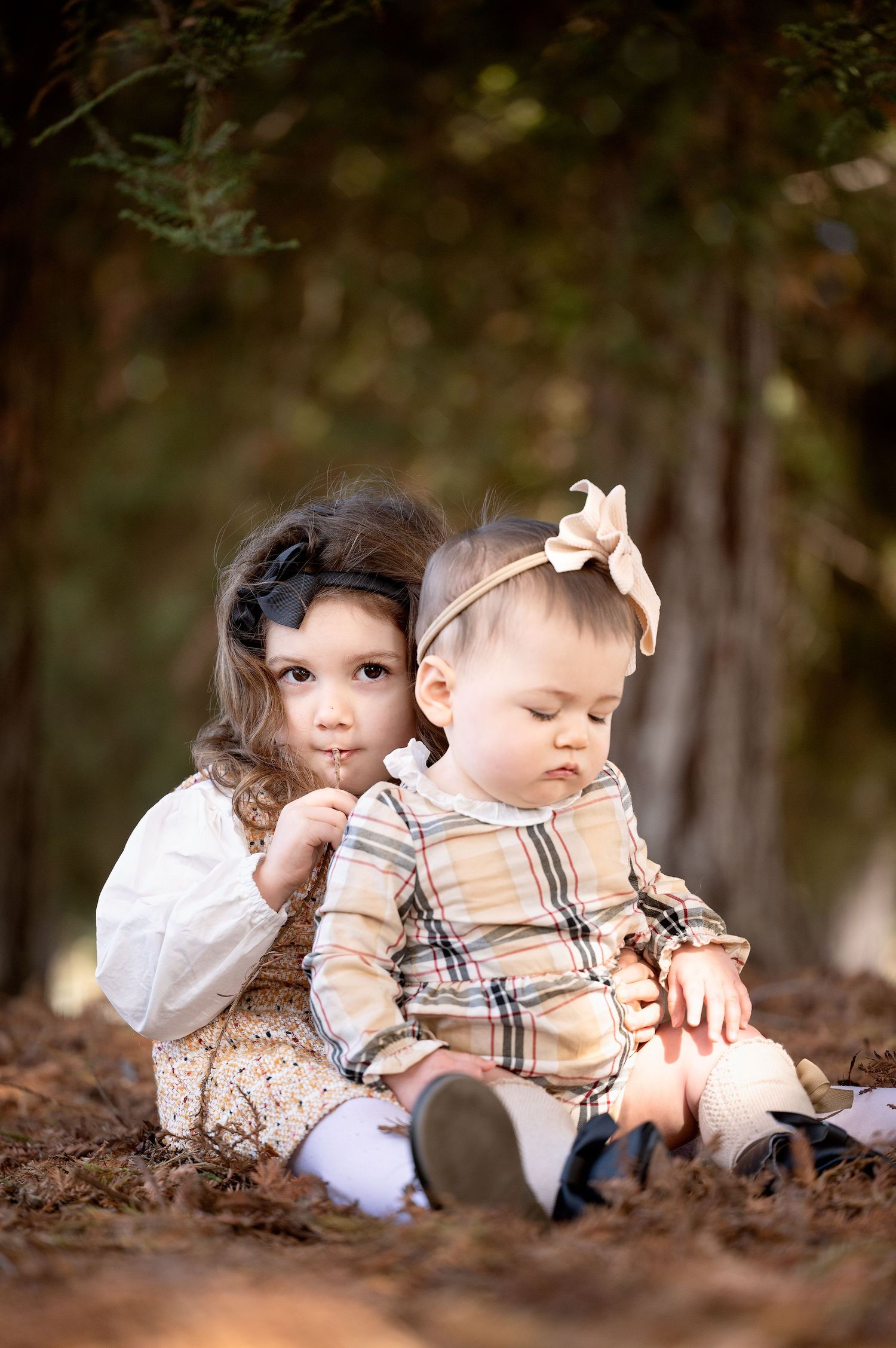 Two young children sit together on fallen autumn leaves in coordinated outfits.