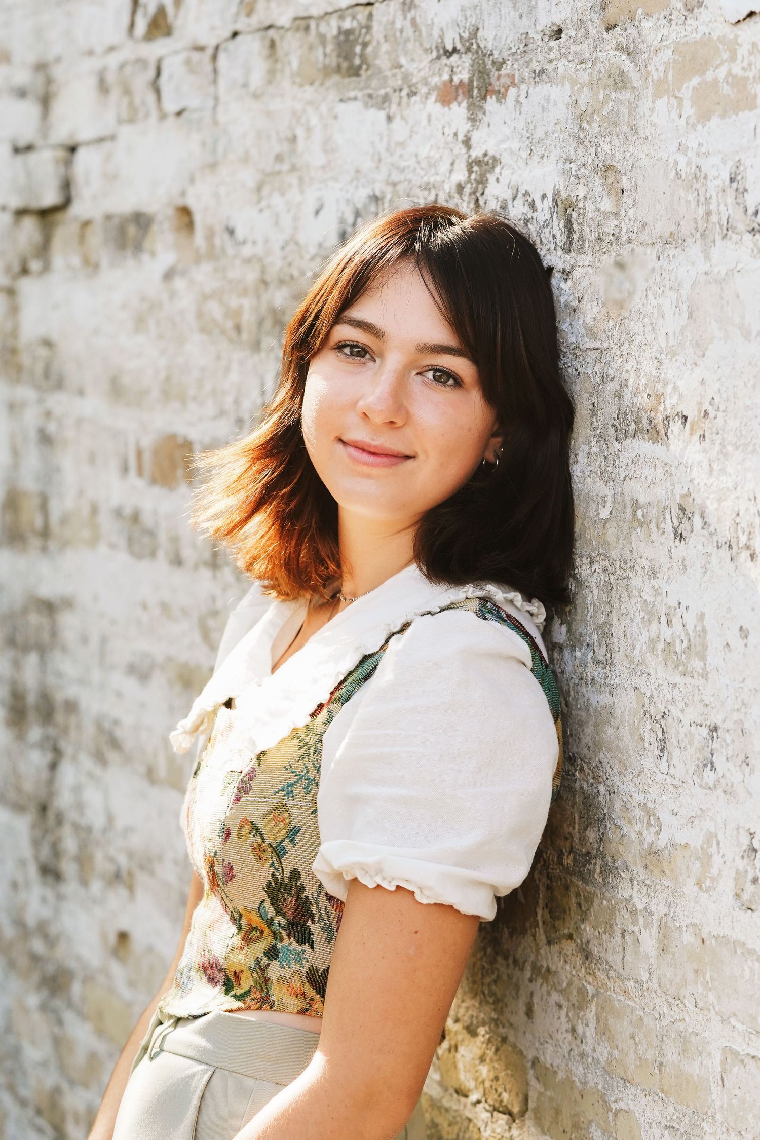 Senior portrait of young girl smiling, back leaned against white brick wall, shot by Milwaukee senior photographer Rachel Dickman.