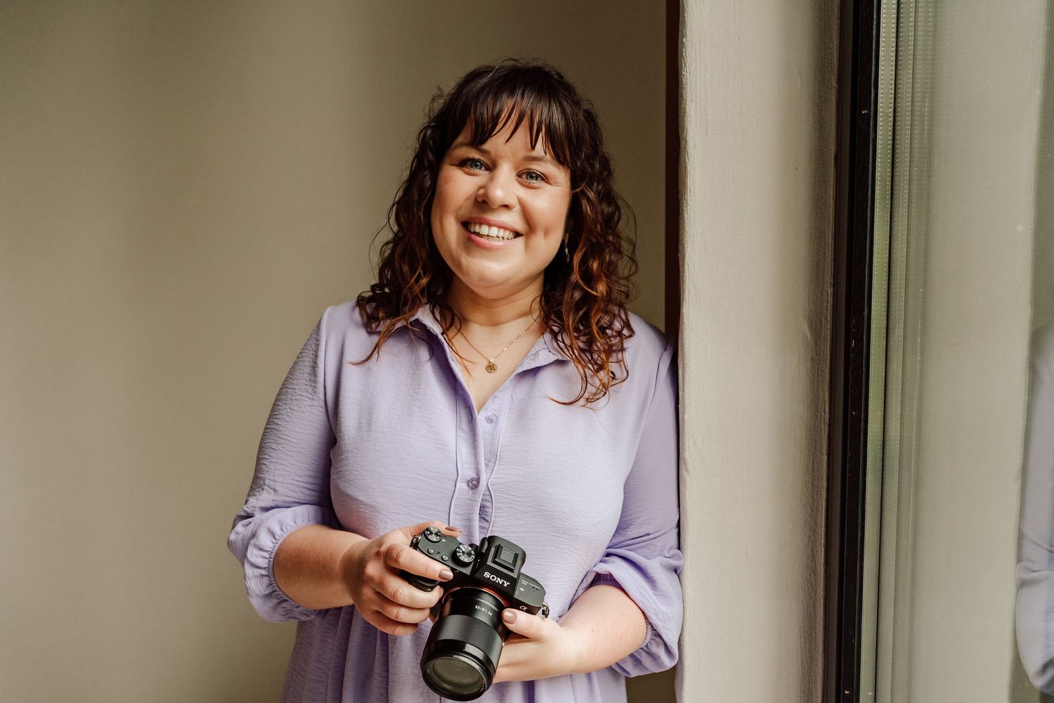 Vrouw moet fototoestel in de hand, lila jurk en leunend tegen de muur