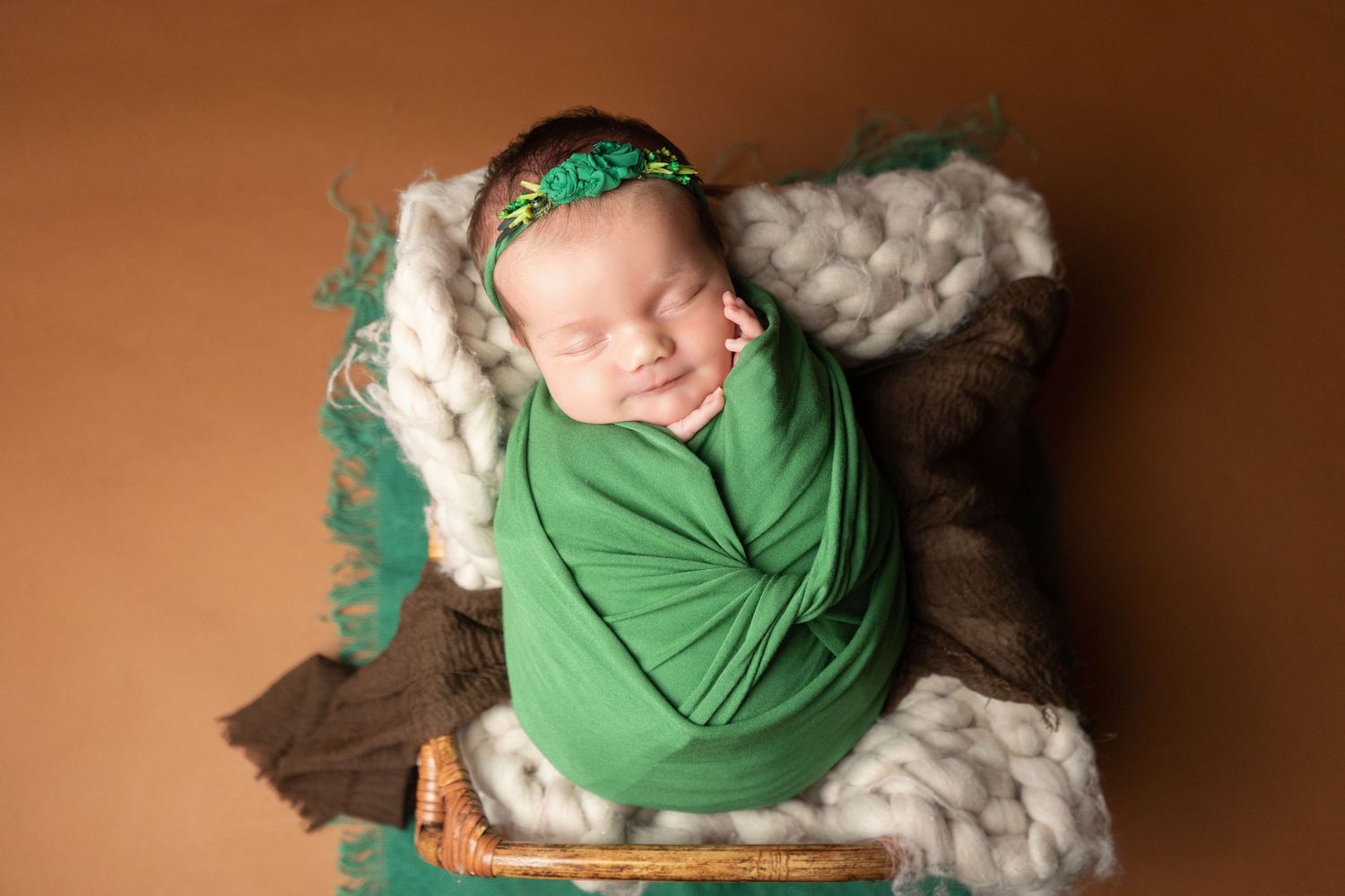 Baby girl sleeping in a wooden bed, wrapped in green with a floral headband at newborn photoshoot in Doncaster.