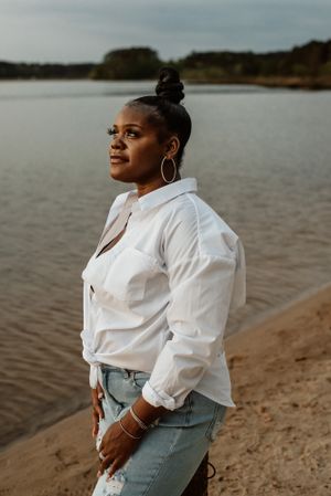 Person in white shirt and jeans poses confidently by a serene lakeside at sunset.