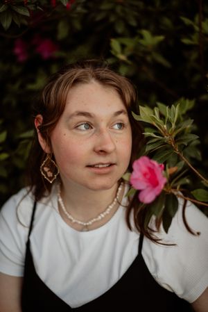 Portrait of a person wearing pearls and earrings near pink azalea flowers.