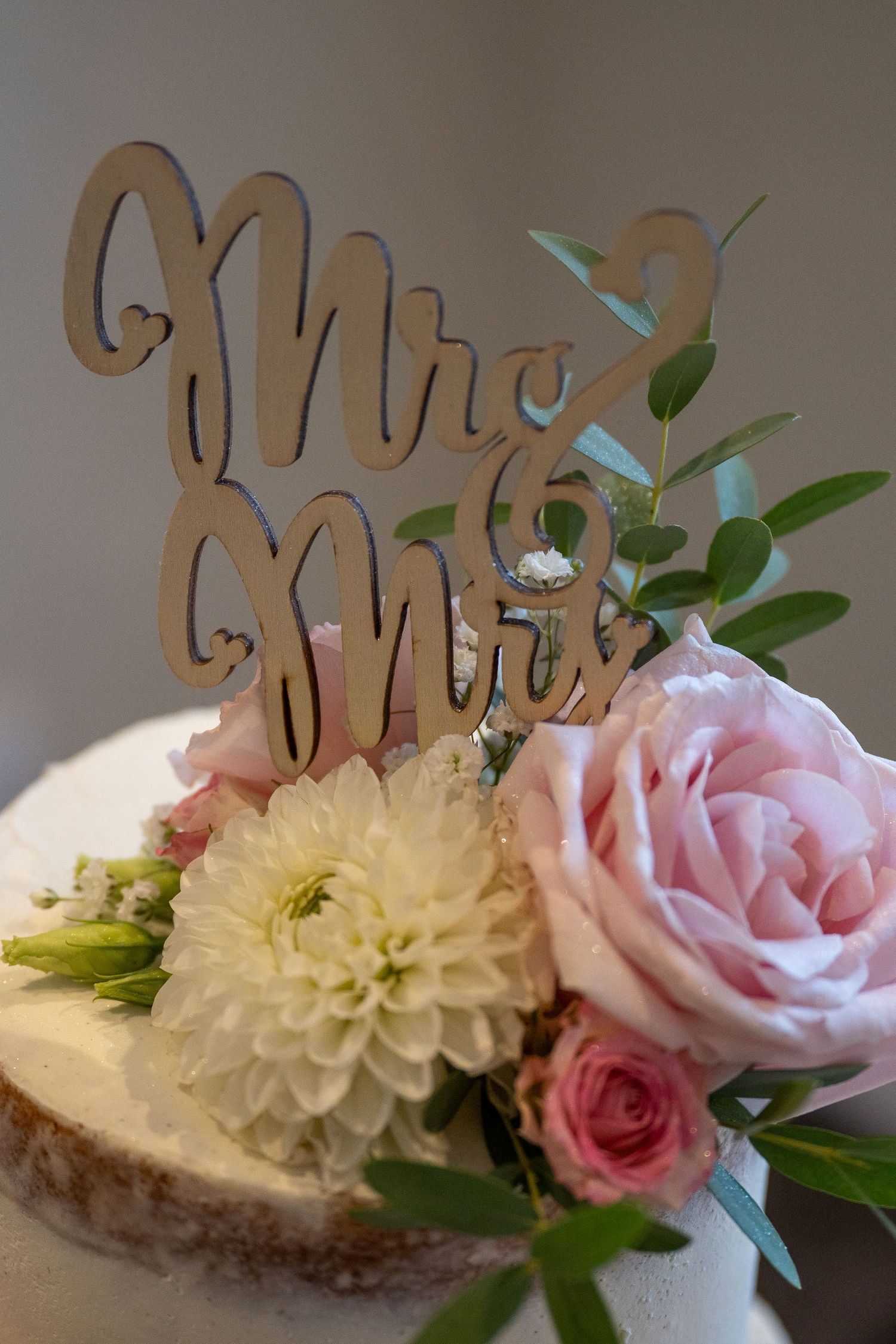 Wedding cake topper reading 'Mr & Mrs' with pink roses and white dahlia flowers.
