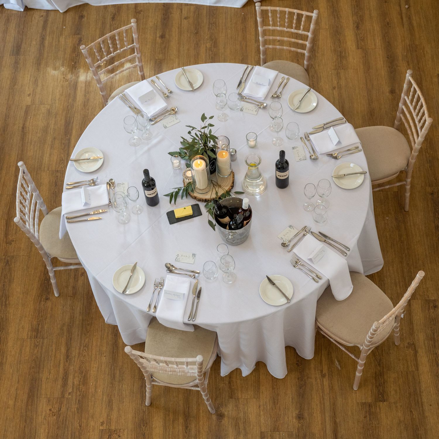Overhead view of a round wedding table with white linens, chiavari chairs and centerpiece decorations.