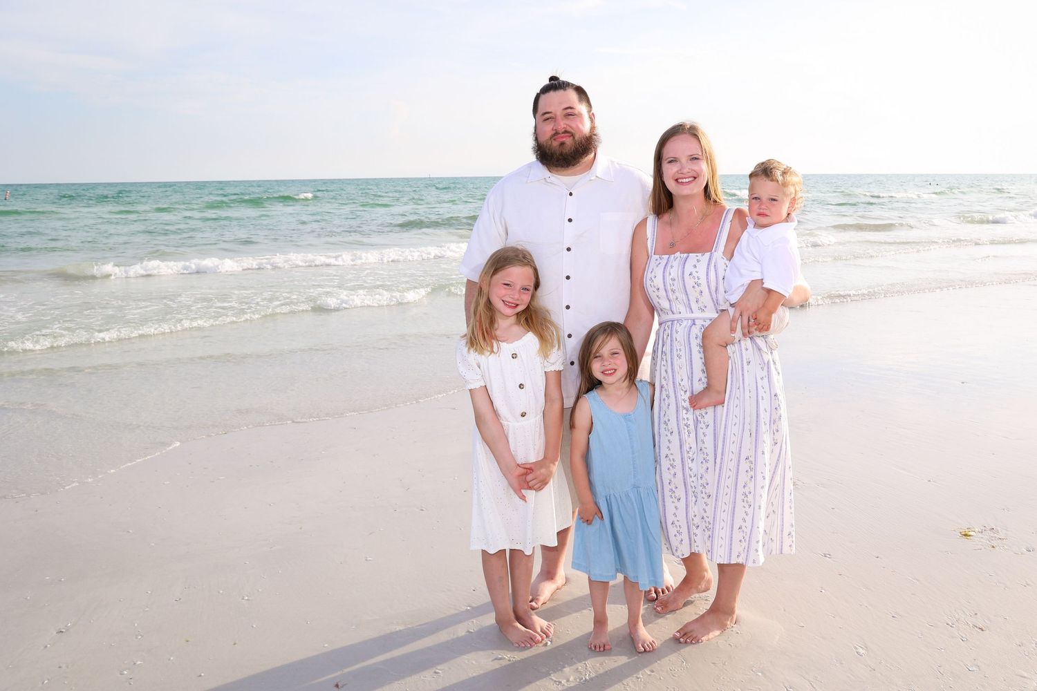 A family dressed in white and blue stands together on a sunny beach.