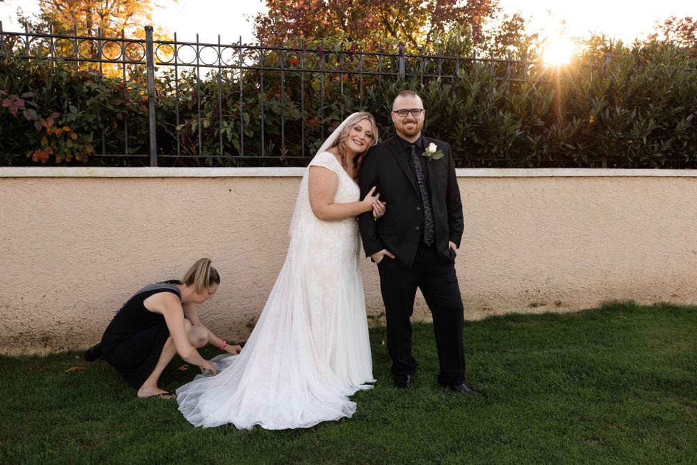 A formal wedding portrait being captured as someone adjusts the bride's dress.