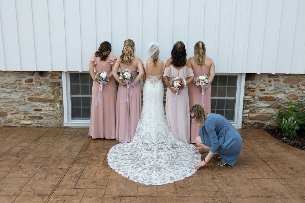 A bridal party in pink dresses helps adjust the lace train of a wedding dress.