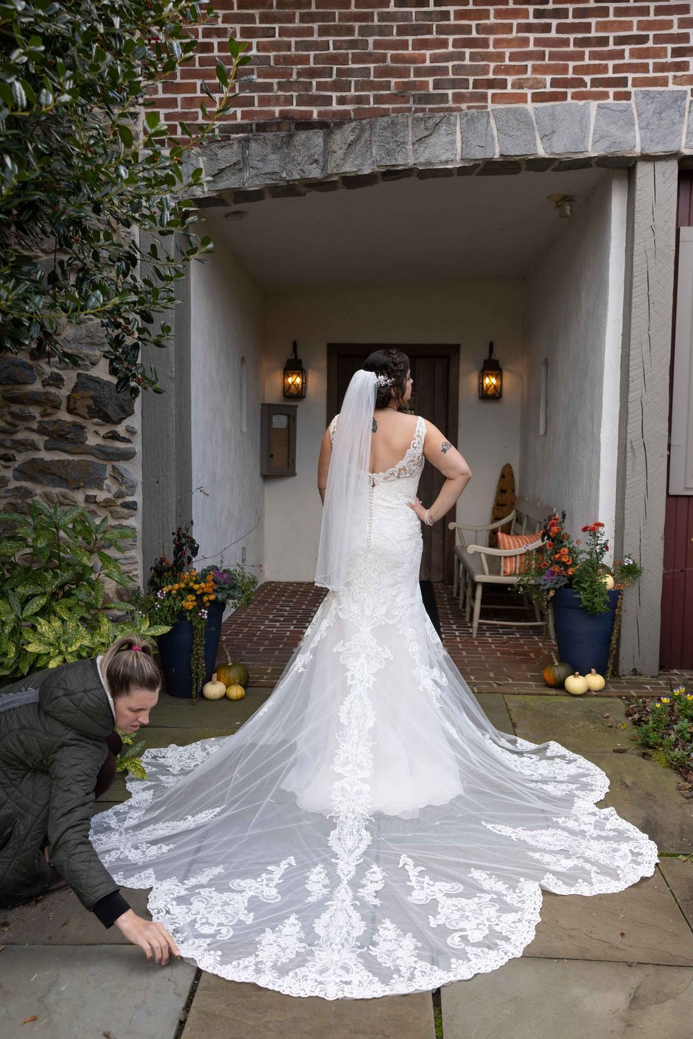 A detailed view of an ornate lace wedding dress train being arranged in a stone archway.