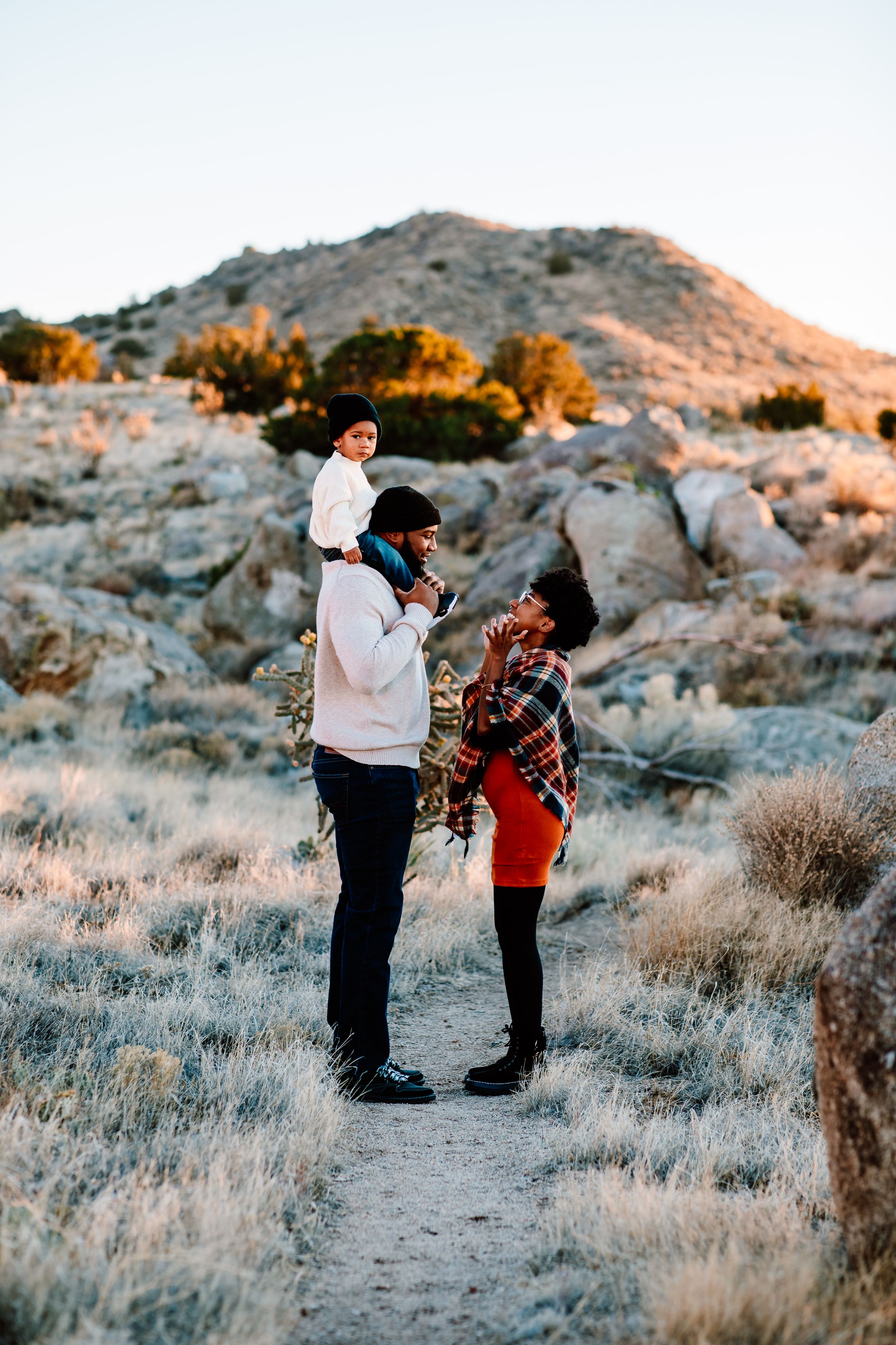 Sweet family interaction on desert path with mountain and brush landscape at sunset.