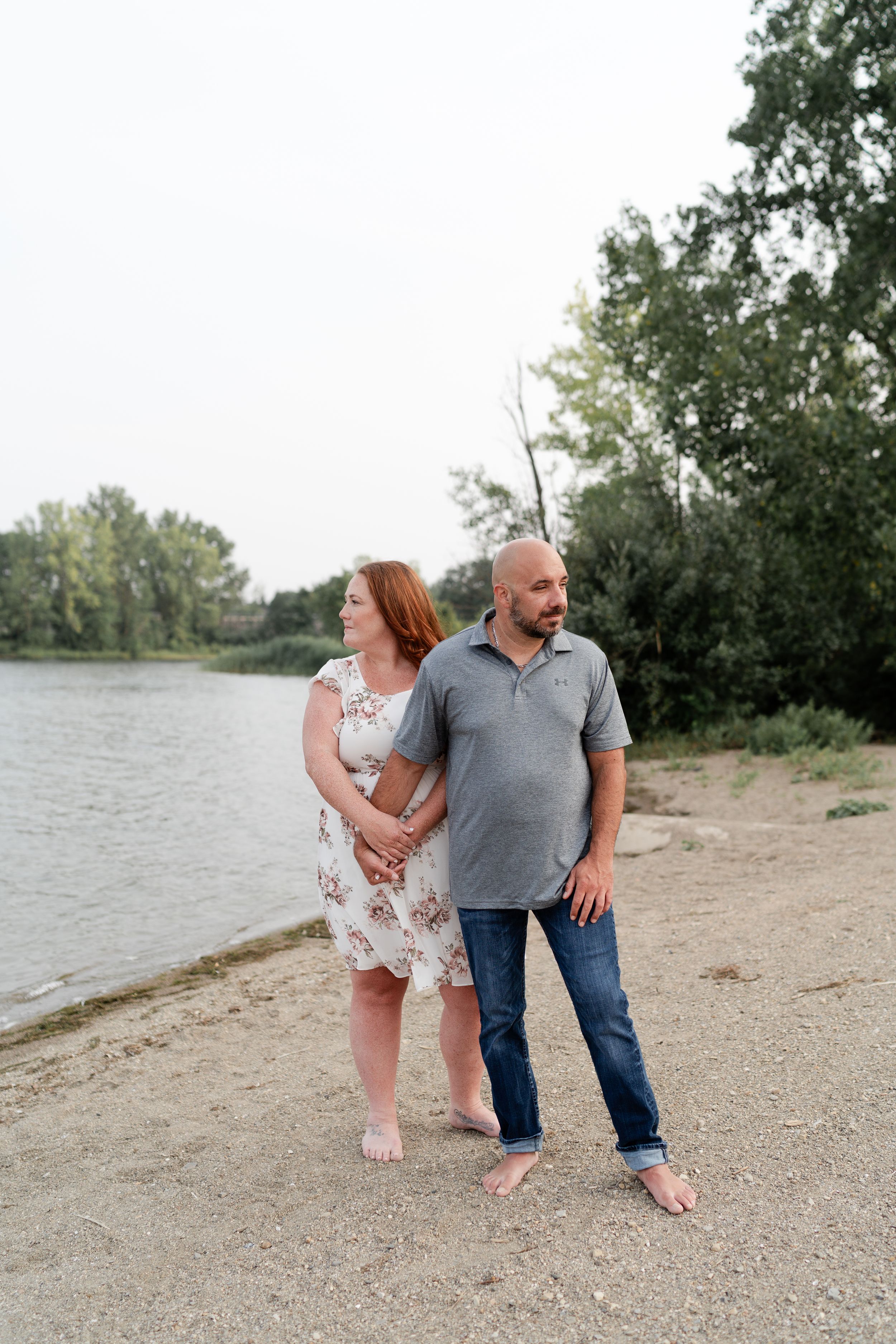 A couple in casual attire walking together along a serene lakeshore.