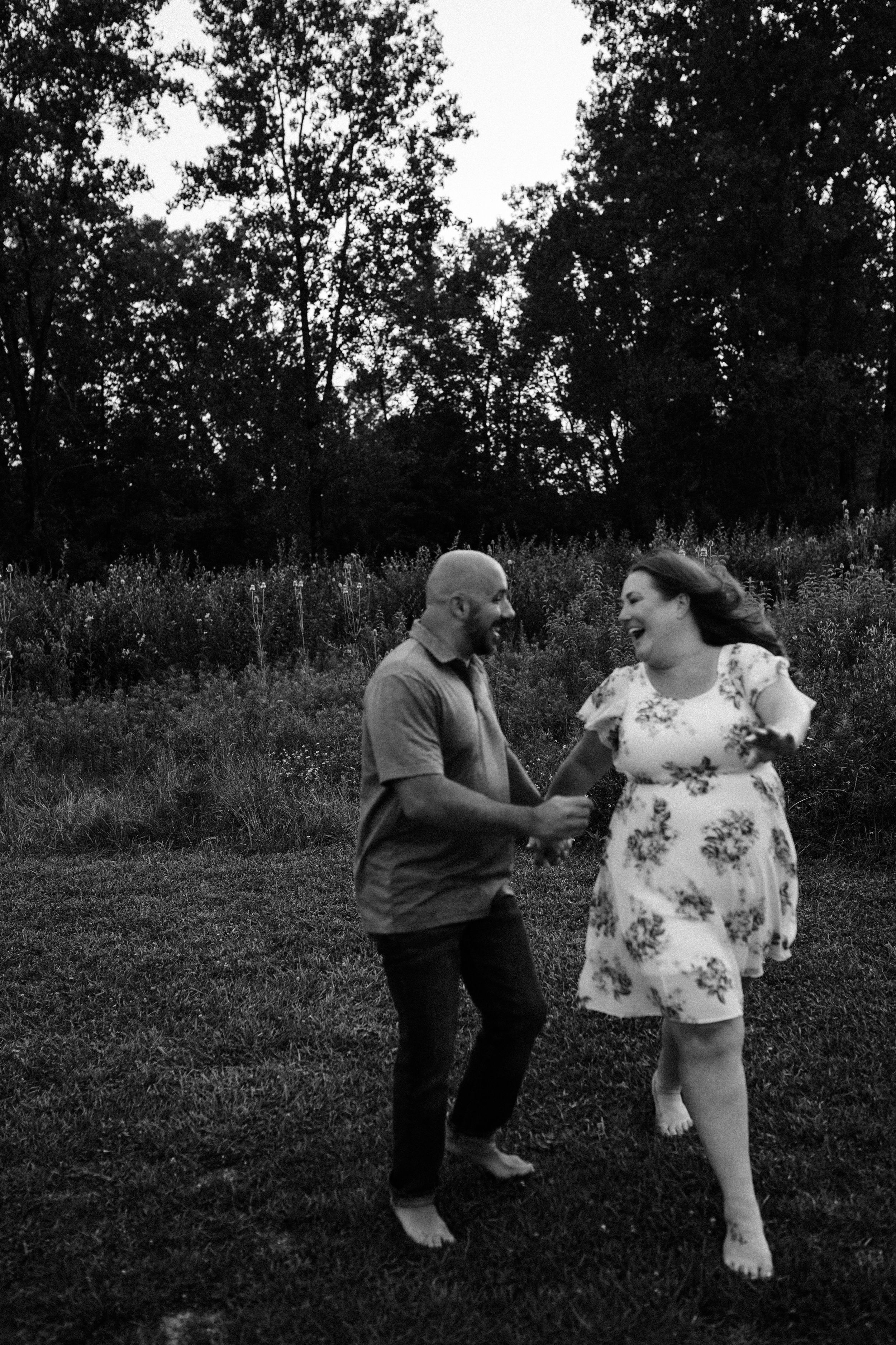 Playful couple dancing barefoot in black and white on grassy field.