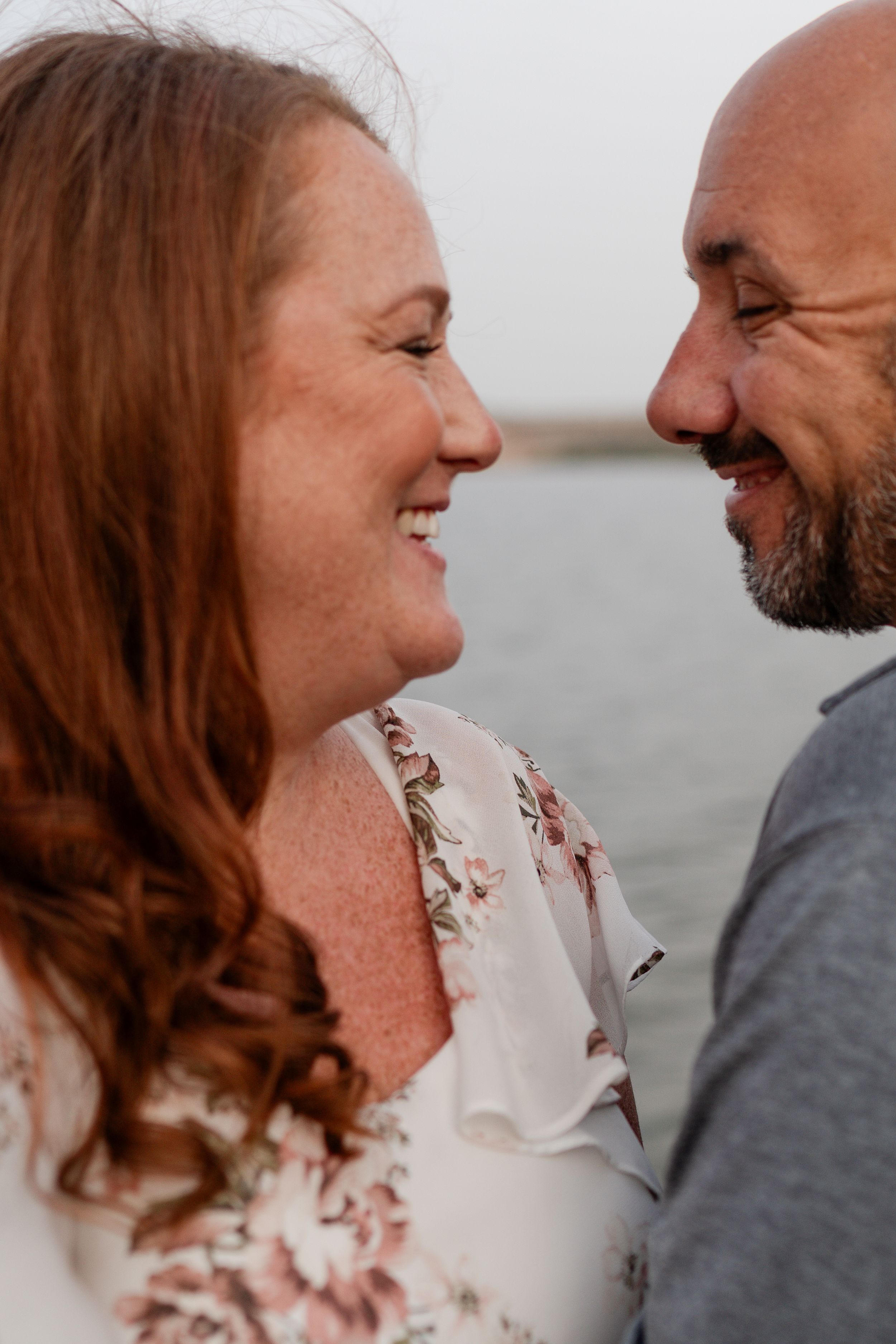 Romantic couple sharing joyful laughter by the waterfront at sunset.