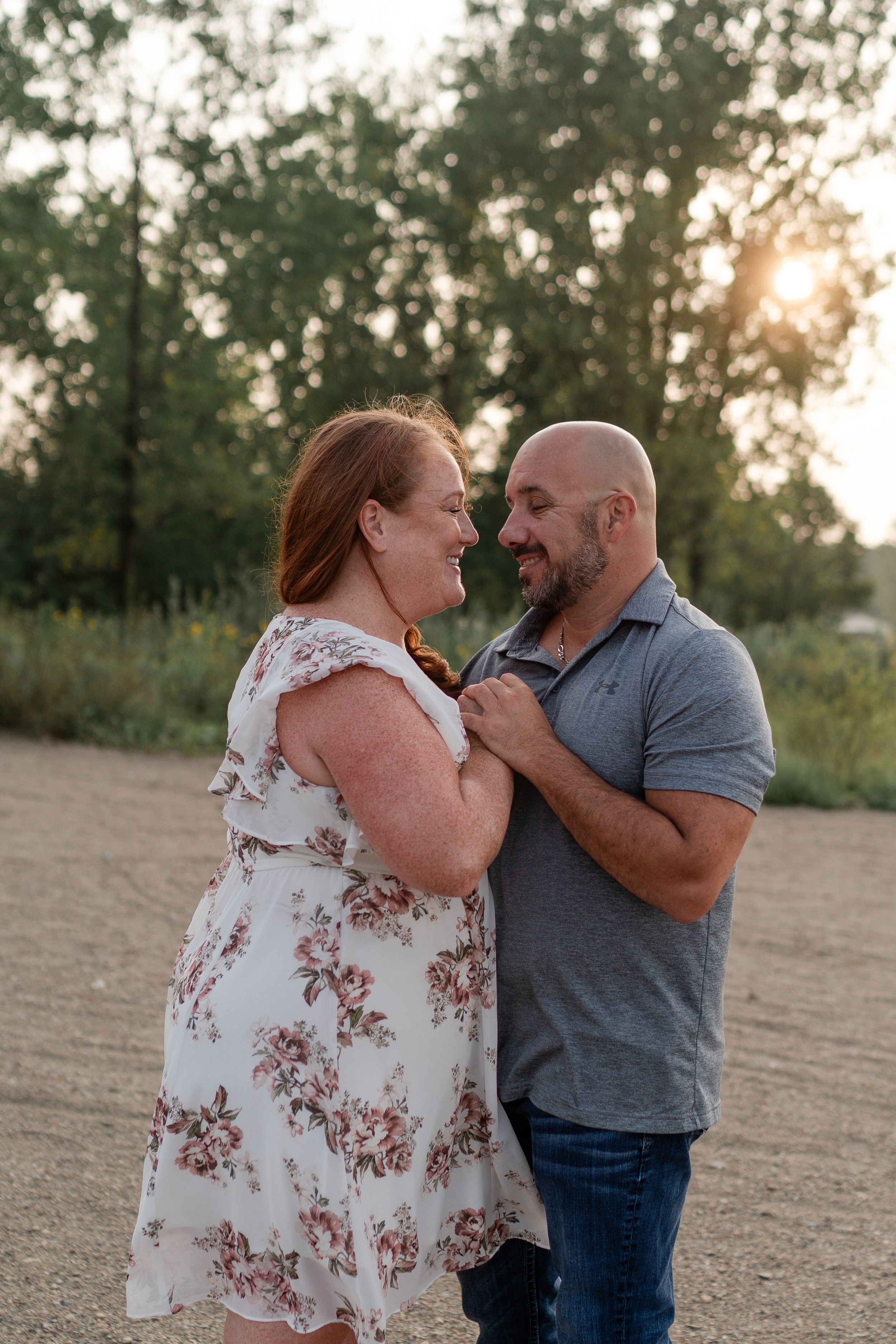 Romantic couple embracing on dirt path with sunlit trees in background.
