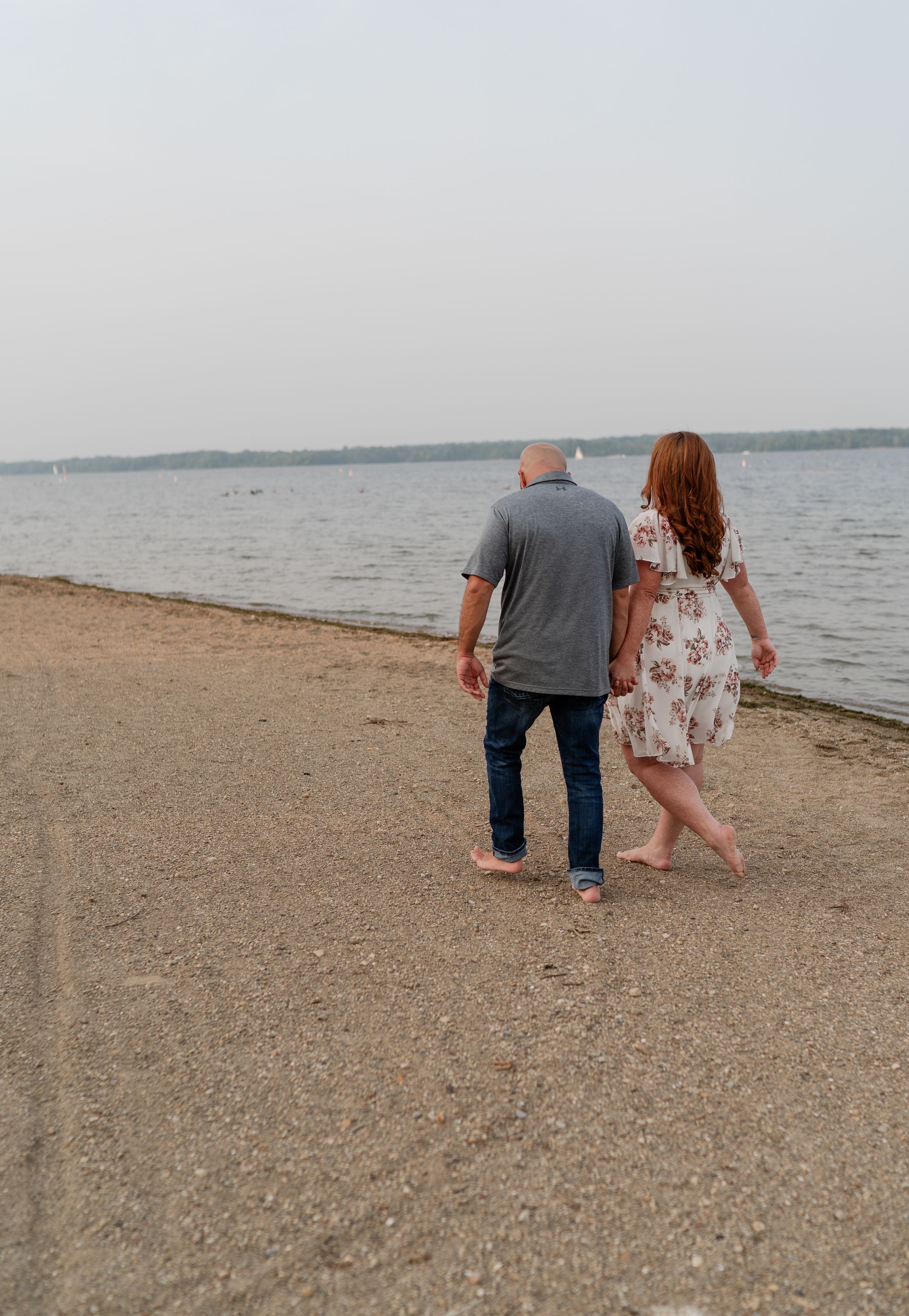 A couple walking away together along a peaceful shoreline at dusk.
