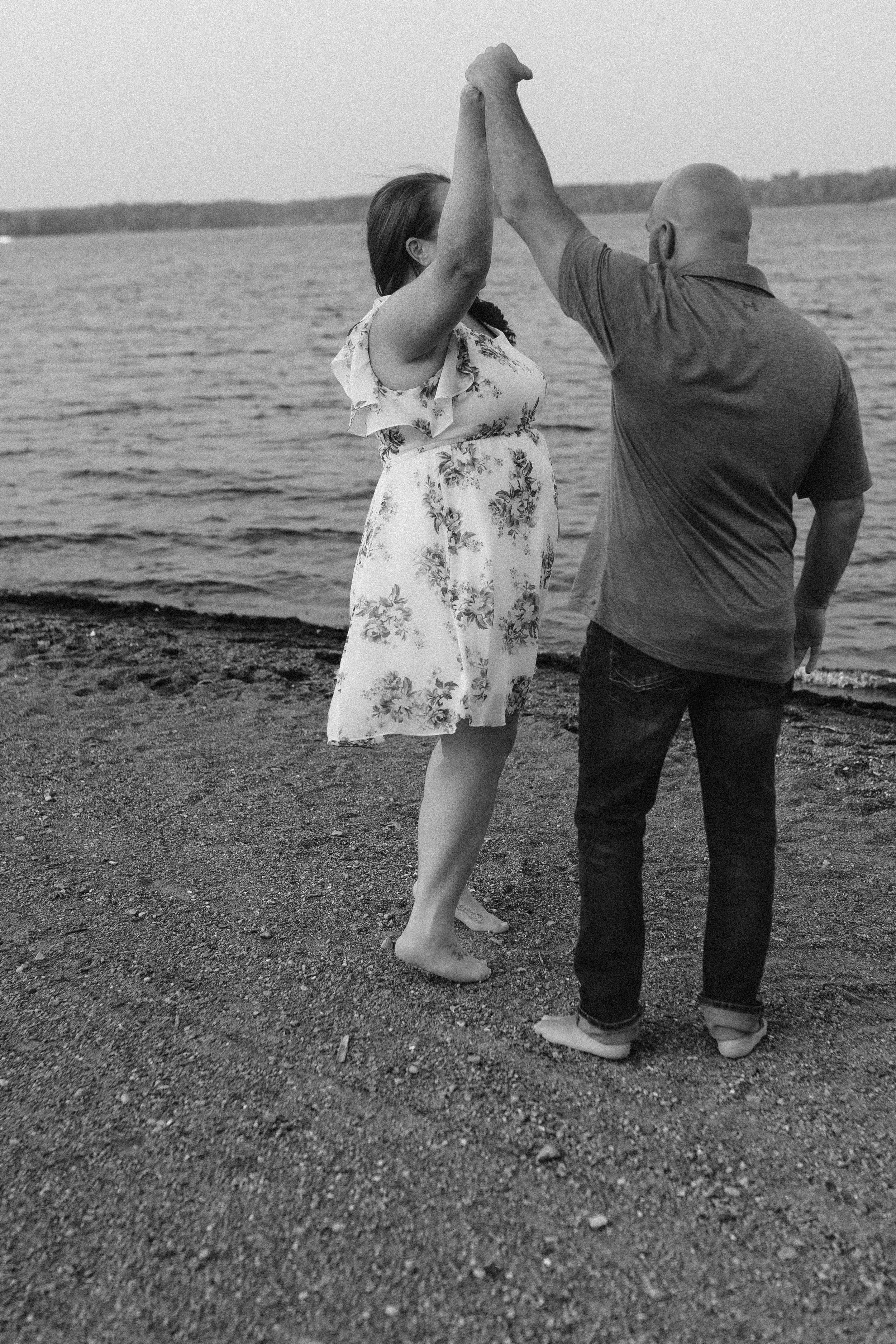 Black and white photo of couple dancing together by the water.