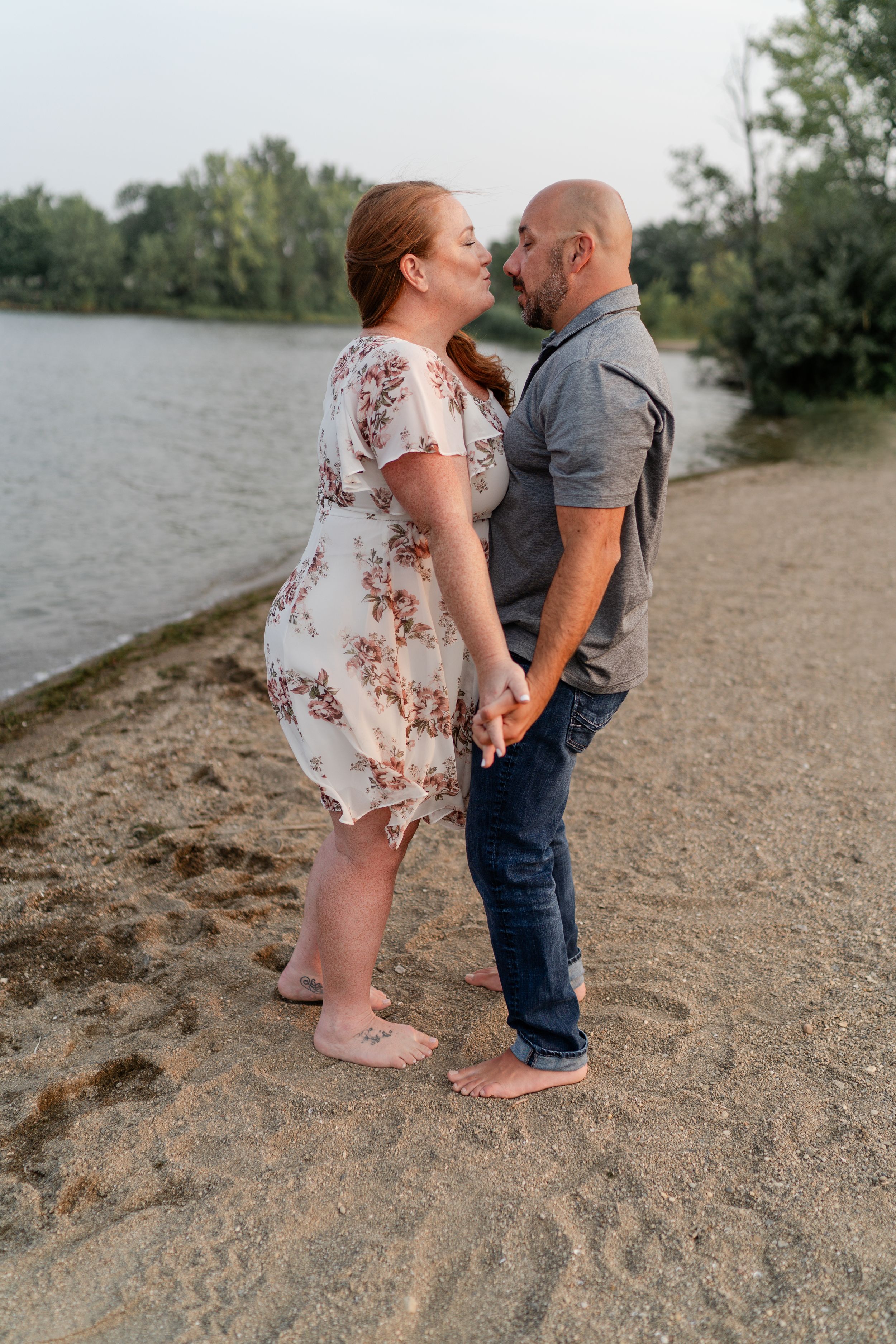 Romantic couple sharing an intimate moment on sandy beach near lake at sunset.