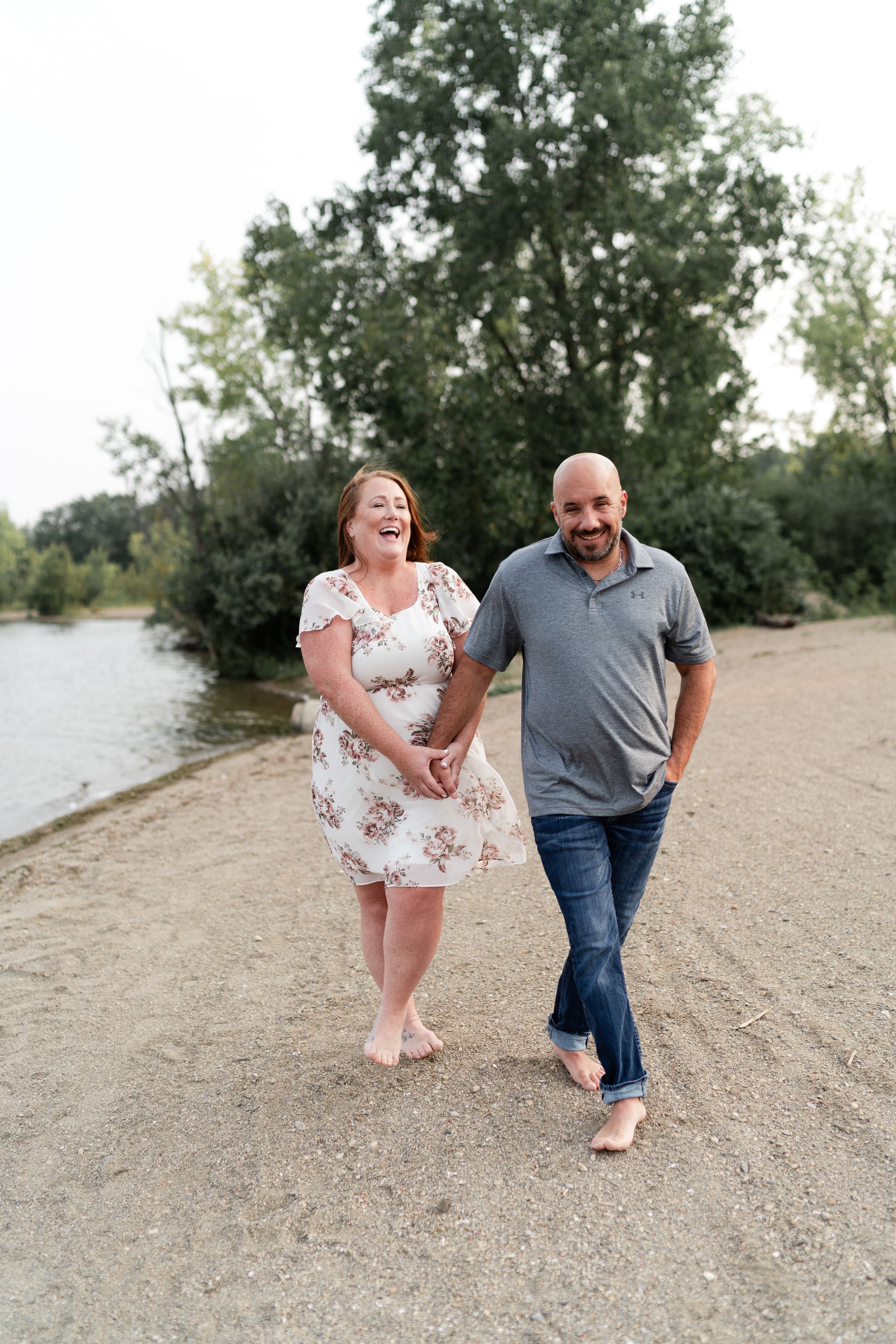 A couple laughing while walking barefoot along a scenic shoreline path.
