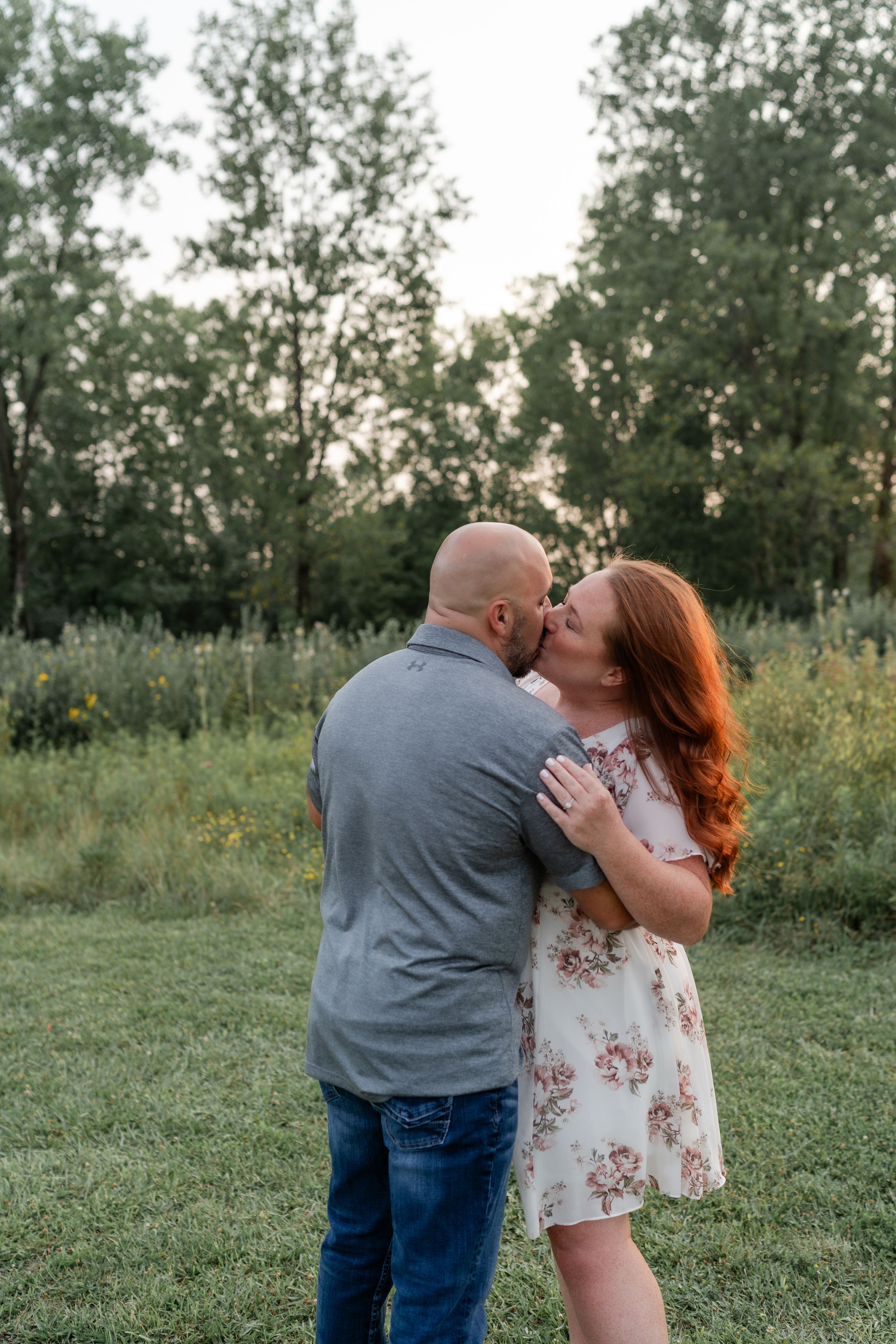Tender embrace between couple in floral dress and grey shirt against nature backdrop.