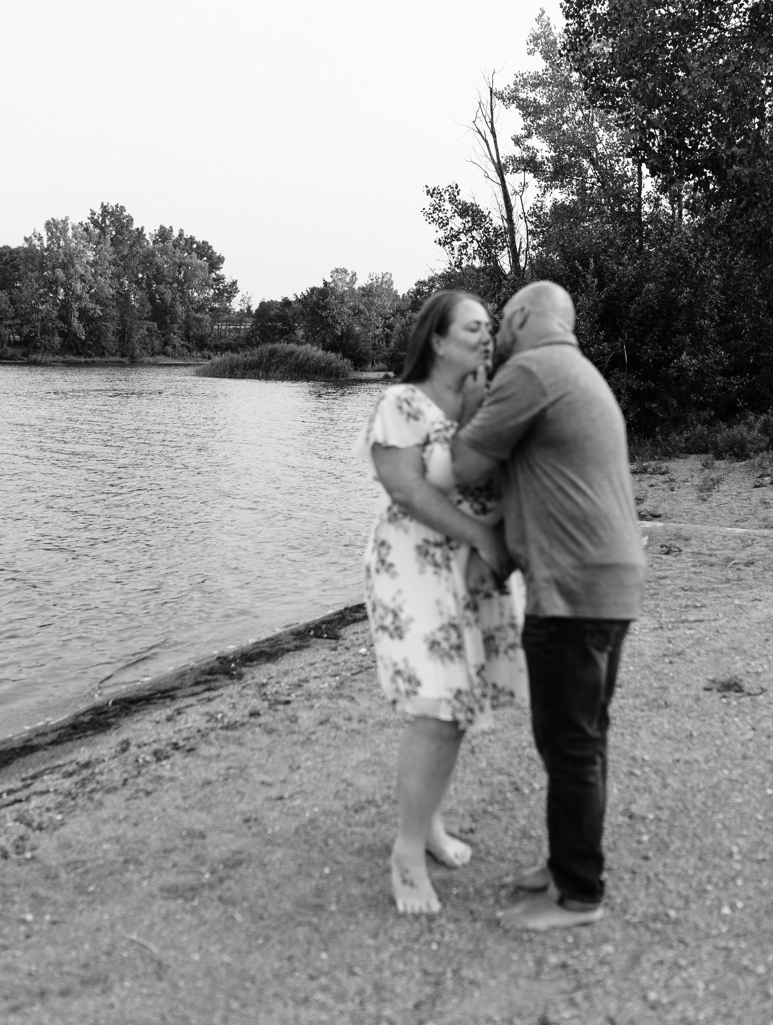 A romantic black and white photo of a couple embracing by the water.