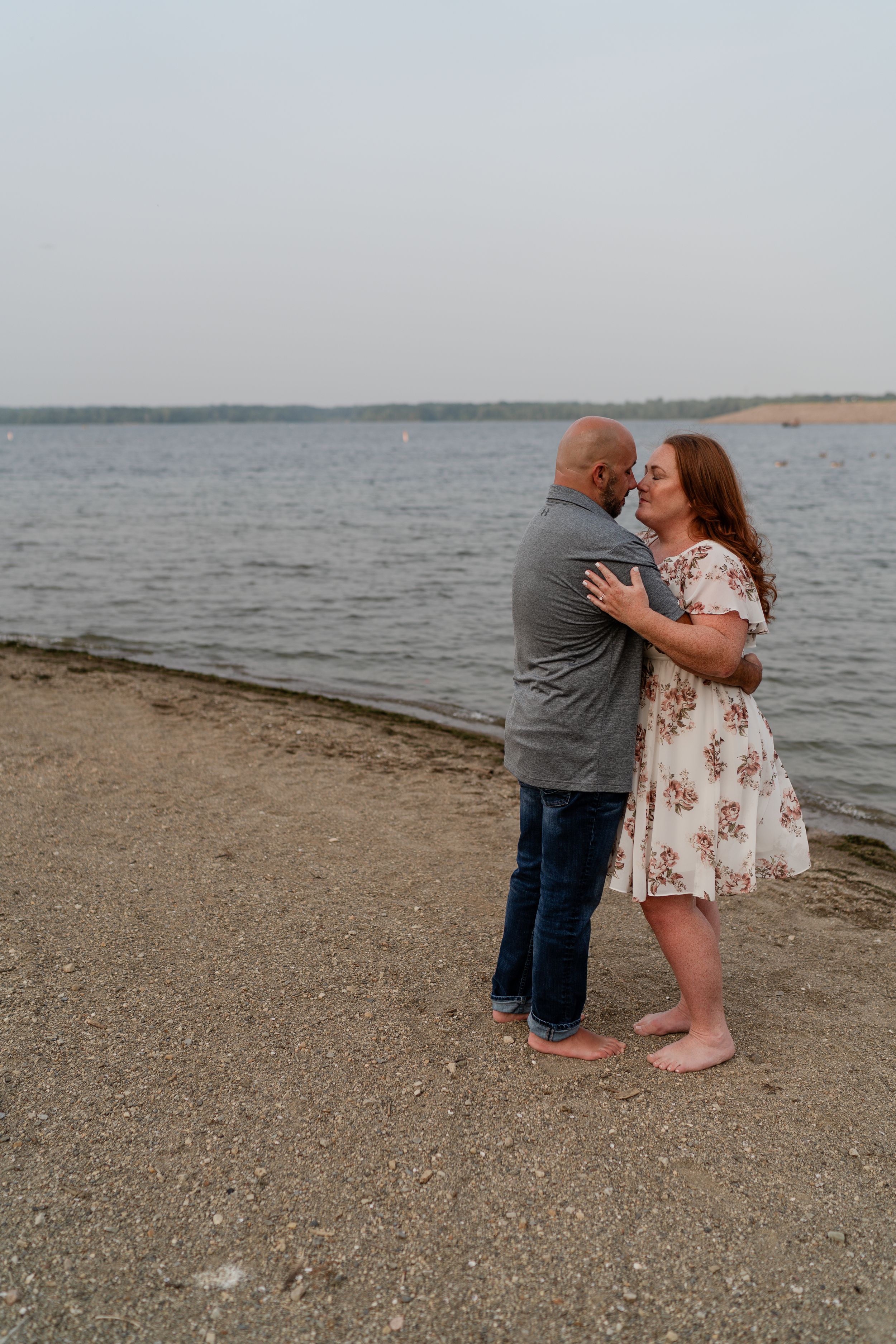 A tender moment between a couple standing on a beach near the water.