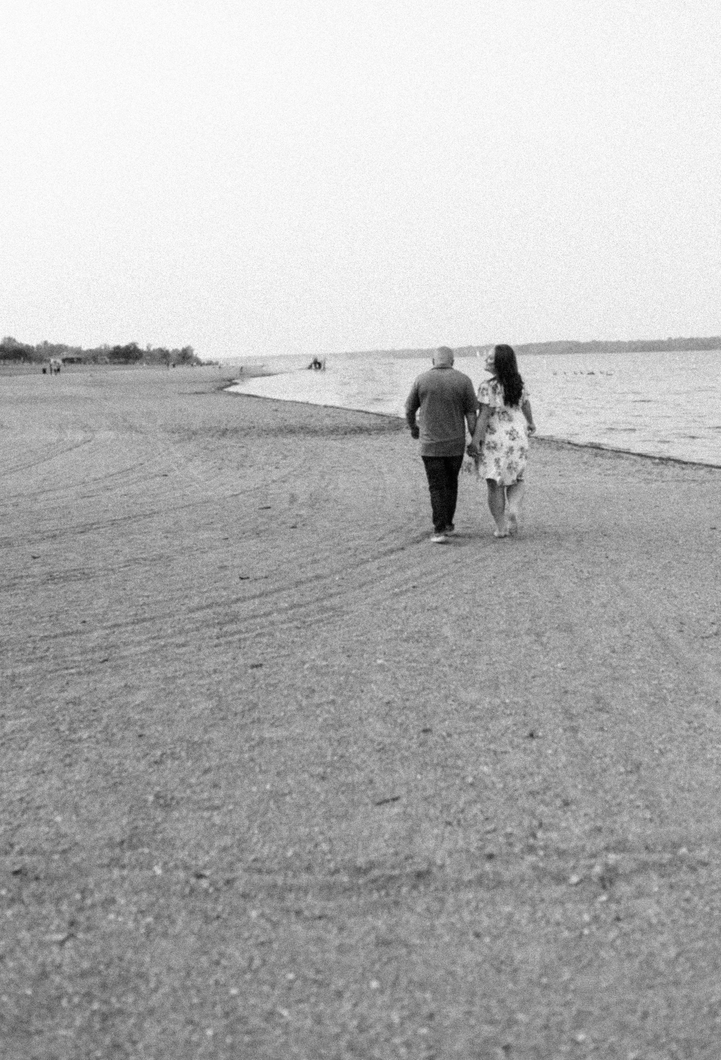 A black and white photo of a couple walking along a peaceful beach shoreline.
