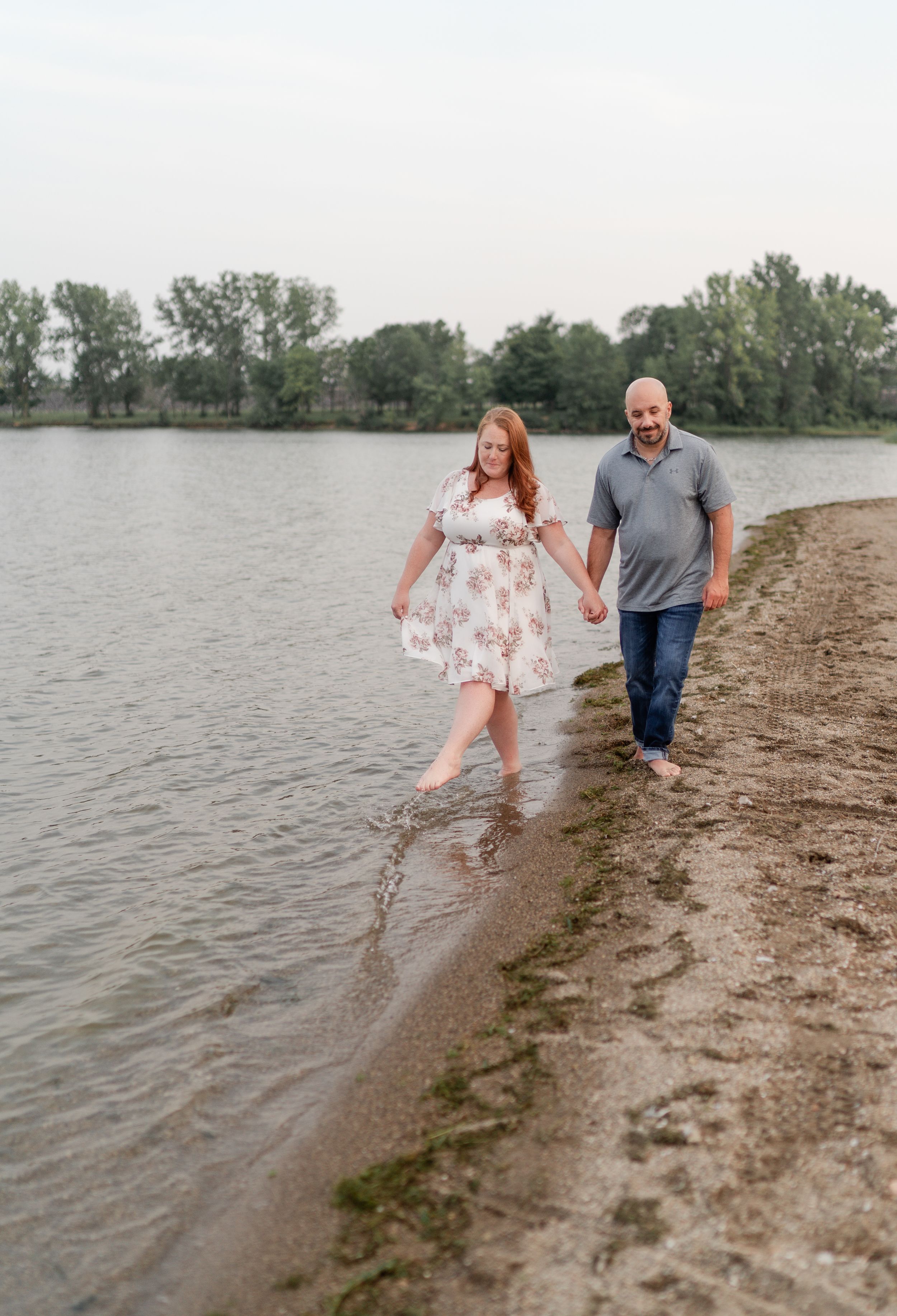Couple walking hand in hand along water's edge at sunset.