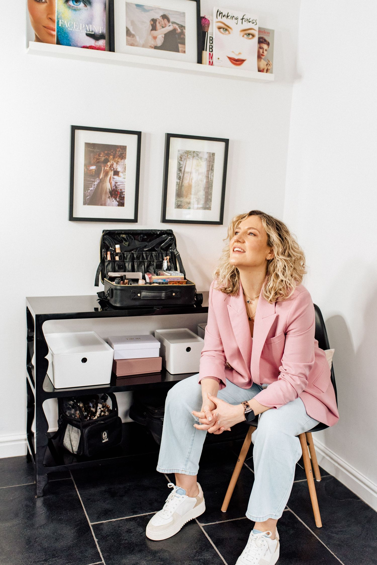 Stylish professional sitting on wooden chair in pink blazer and jeans in modern office space.