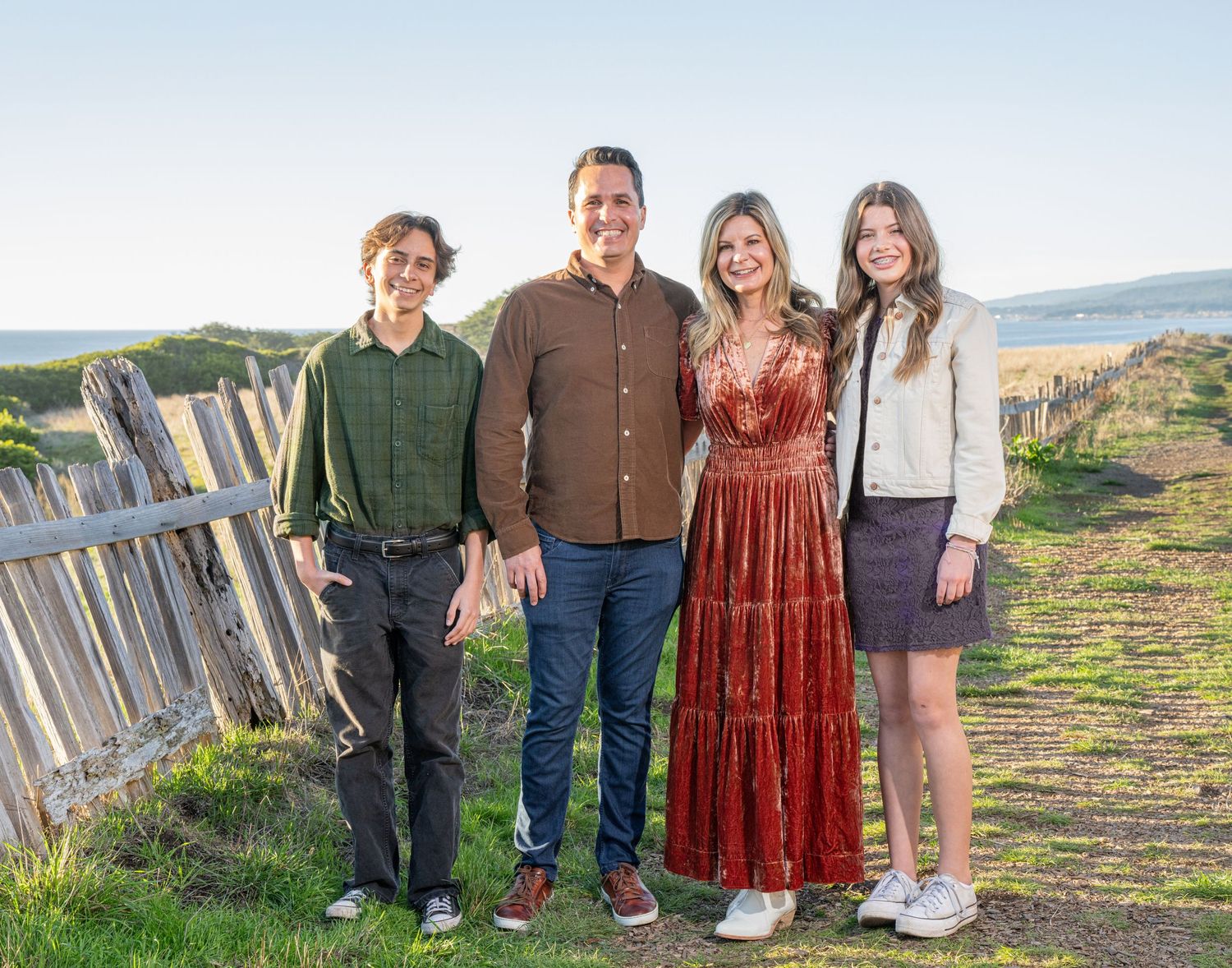 Four people stand together outdoors against a rustic fence and rolling landscape background. At The Sea Ranch Lodge in Northern California.