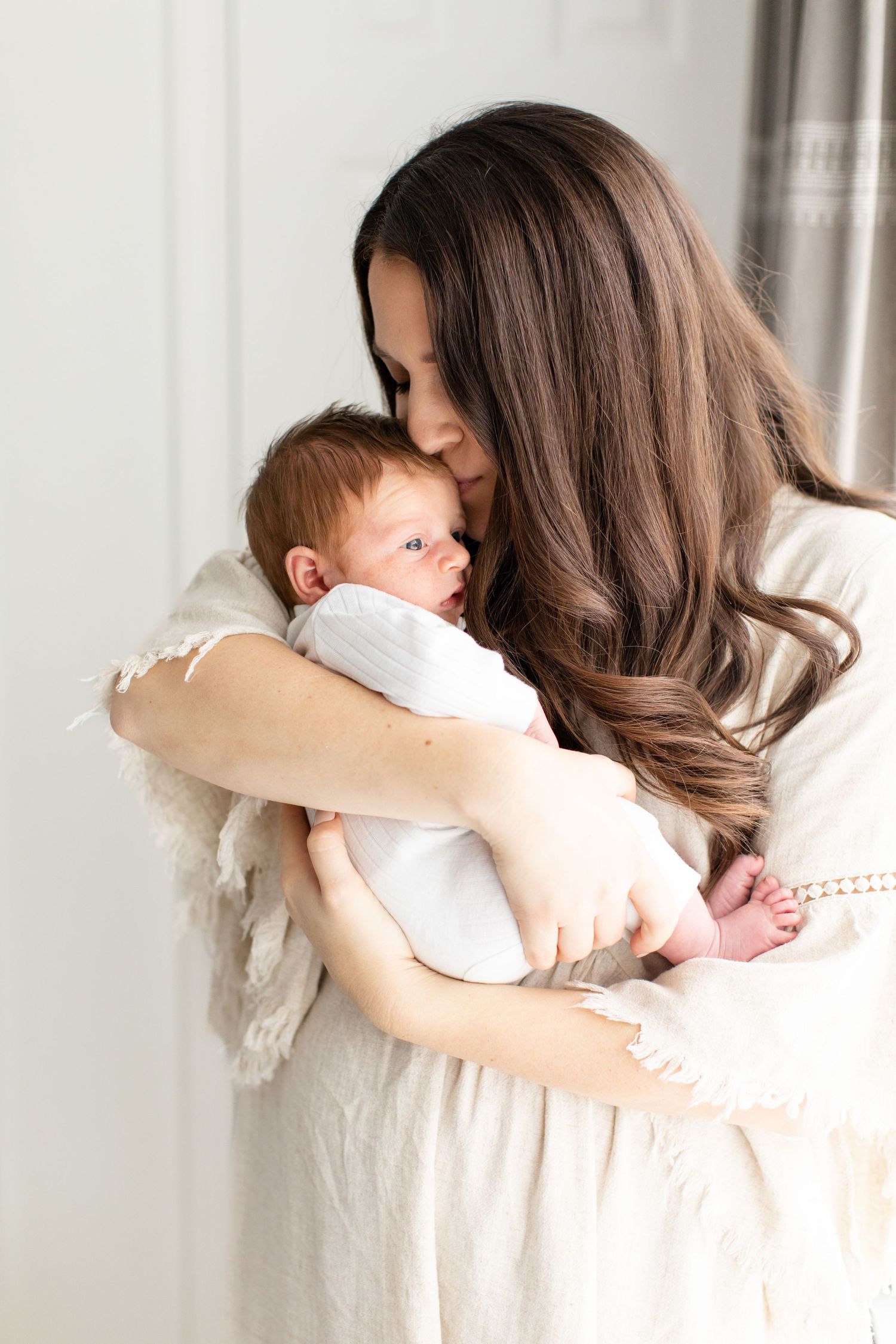 A sweet moment captured as parent cradles newborn in natural light against white door.