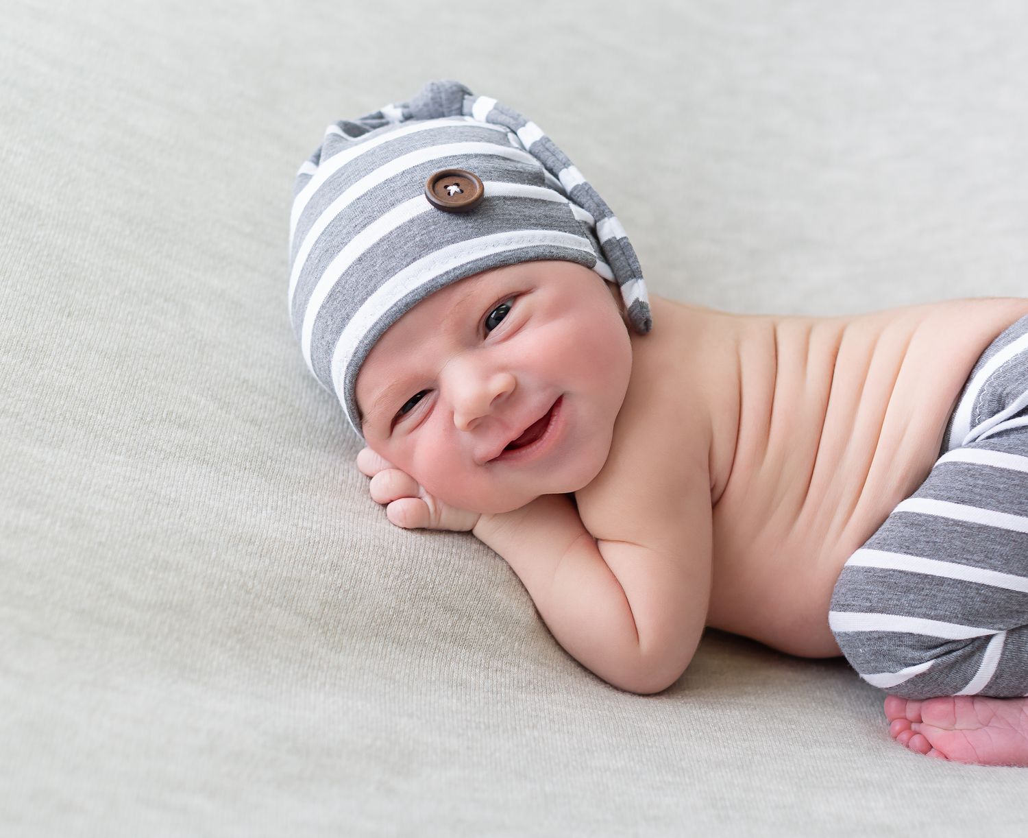 Series of photos showing a baby lying on a grey blanket wearing a striped hat.