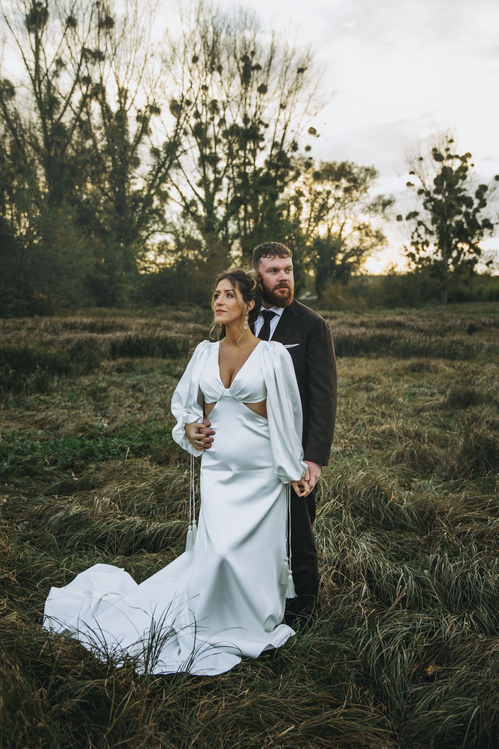 Elegant wedding portrait in field at sunset with flowing white dress.