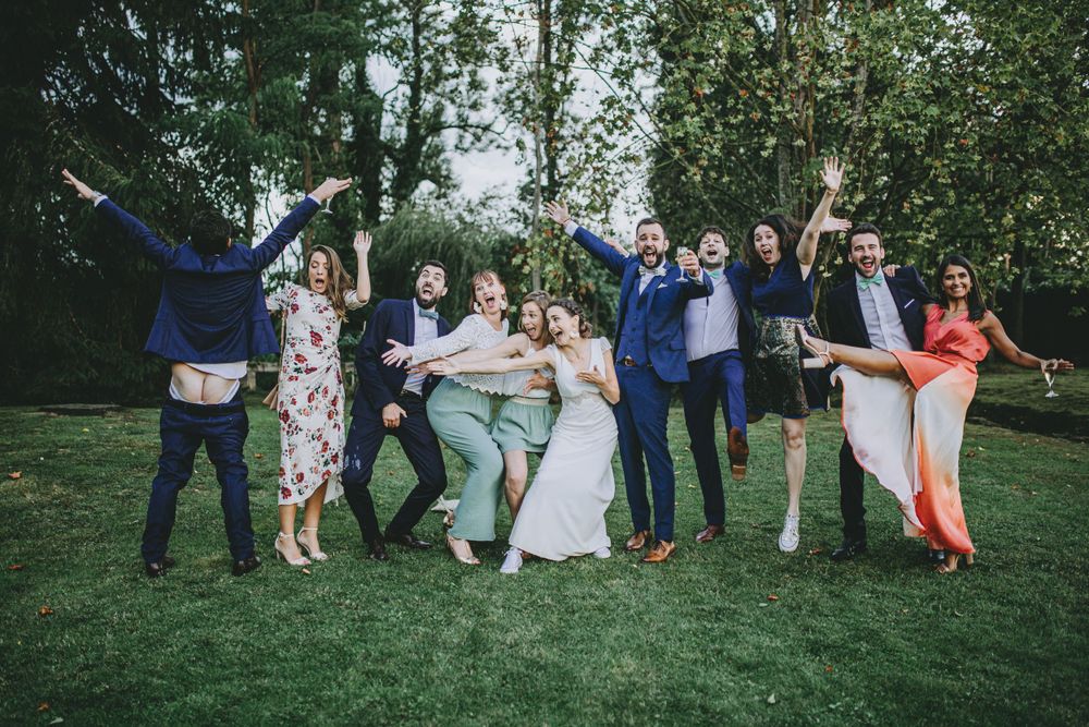 Large wedding party gathered on grass for fun group photos during outdoor reception.