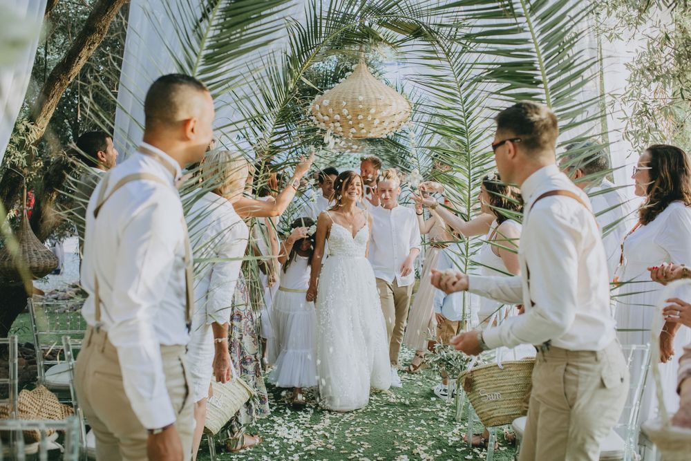 Wedding party dressed in white celebrating outdoors under palm trees.