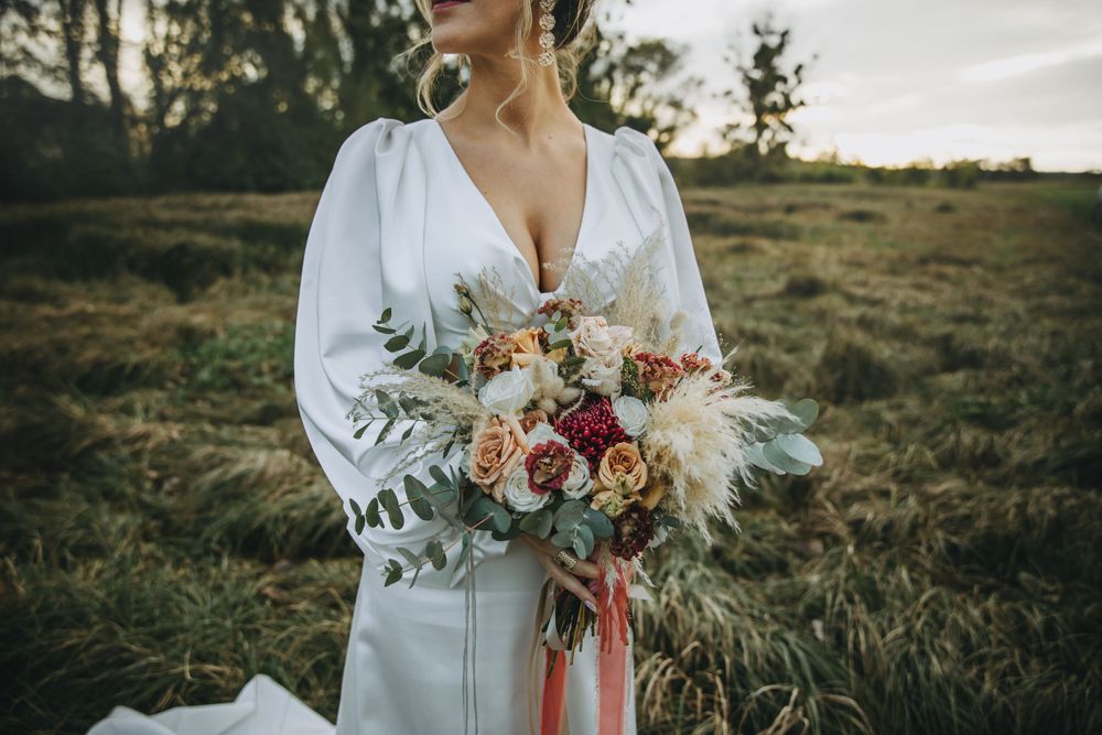 A beautiful bridal bouquet with pink and peach flowers and eucalyptus leaves against a natural outdoor backdrop.
