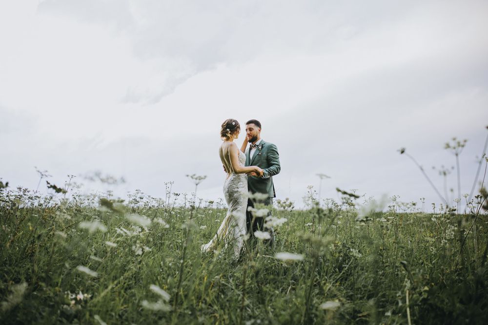 Wide landscape view of a couple walking through a wildflower meadow on their wedding day.