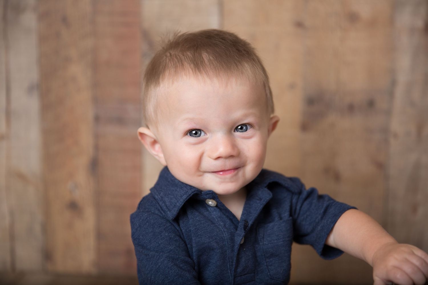 Young child wearing navy blue shirt poses against rustic wooden background.