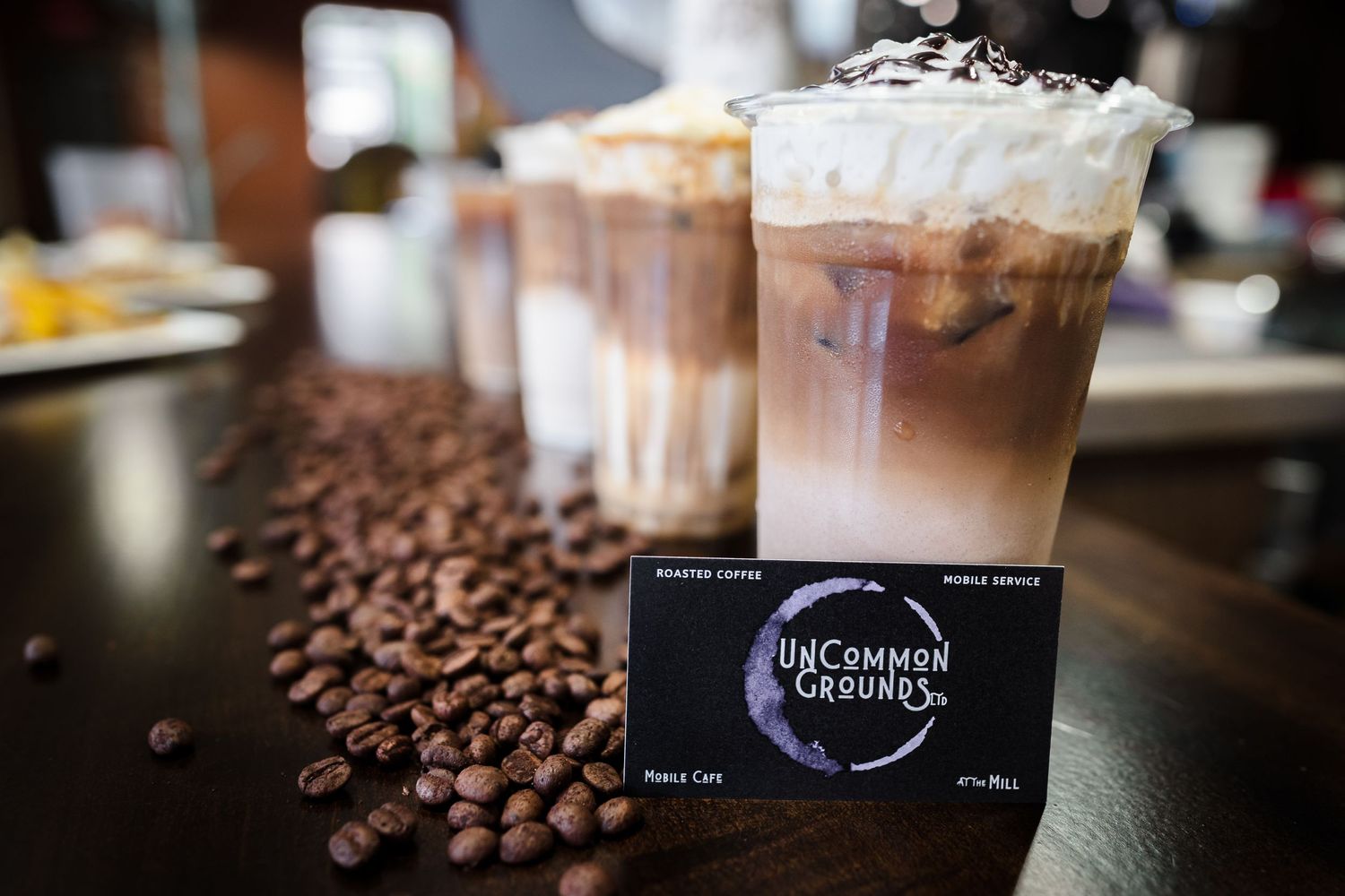 Coffee drinks with whipped cream and coffee beans displayed with an Uncommon Grounds card.