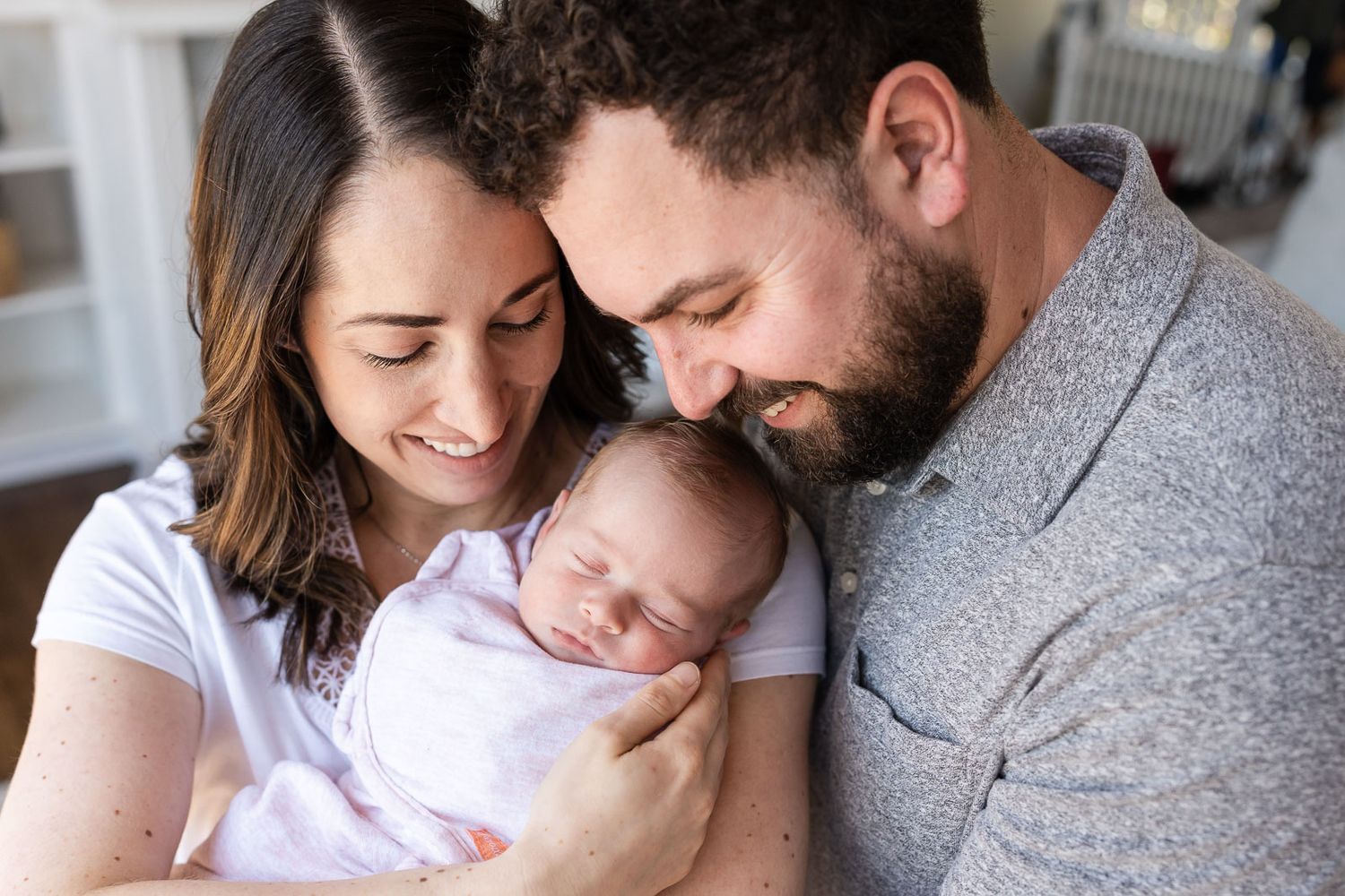 Family photo of parents smiling at newborn daughter.