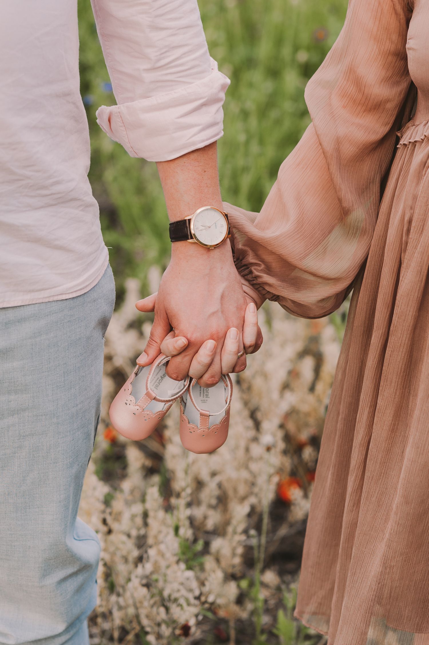 Close-up of hands holding small baby shoes in a garden setting.