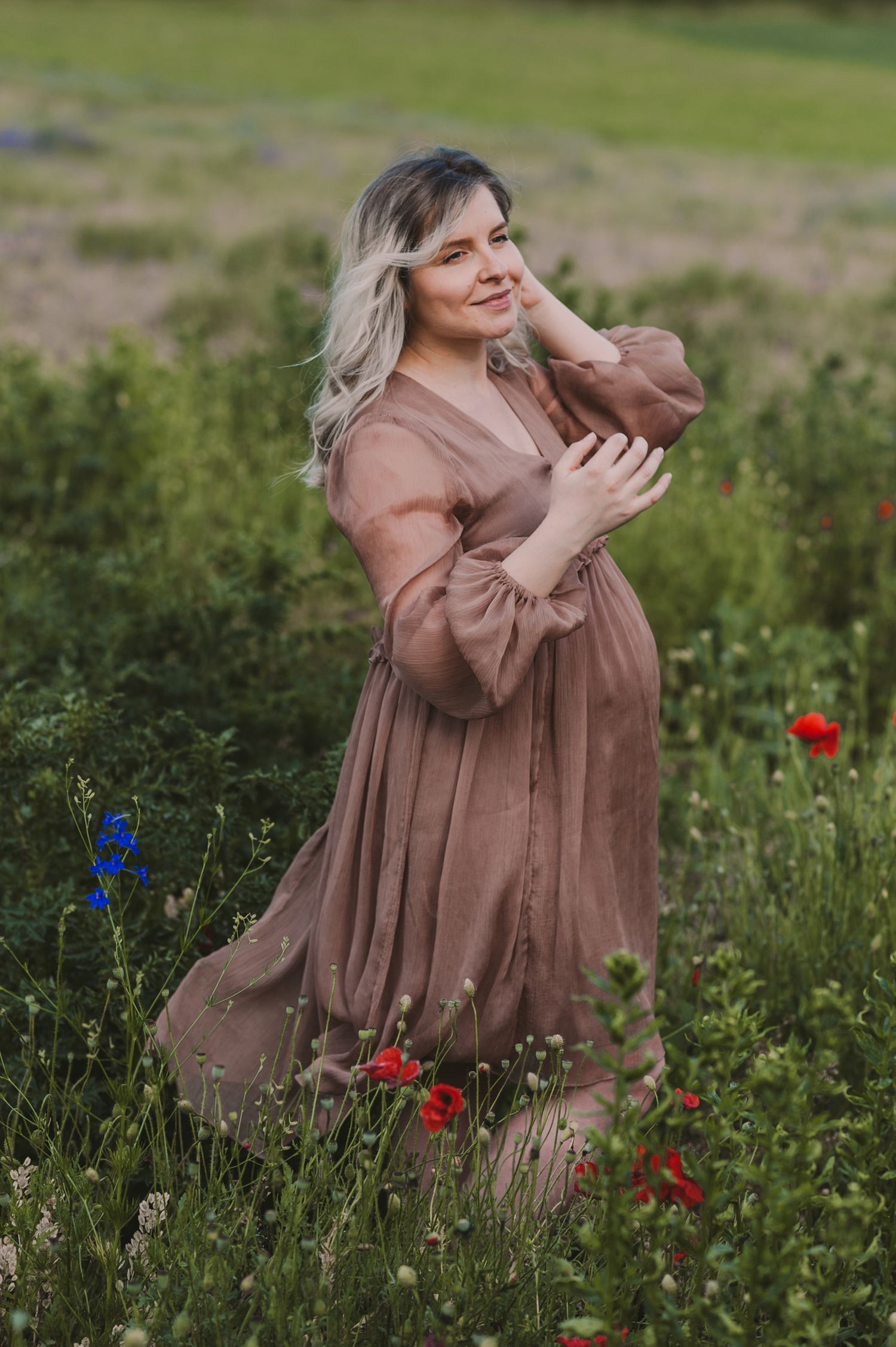 Woman in brown flowy dress twirling in a wildflower meadow with red poppies.