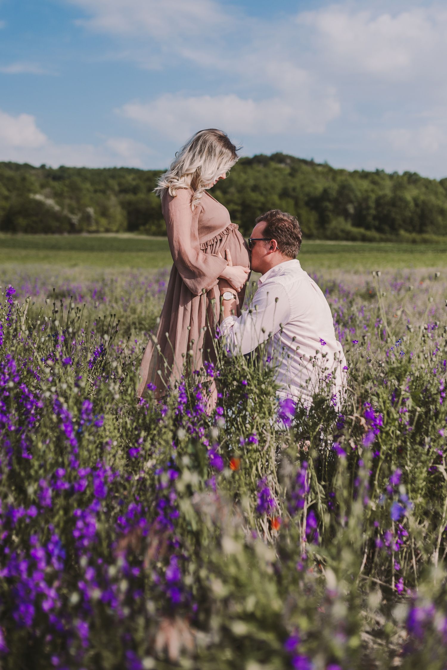 Couple embracing in a beautiful field of purple wildflowers under blue sky.