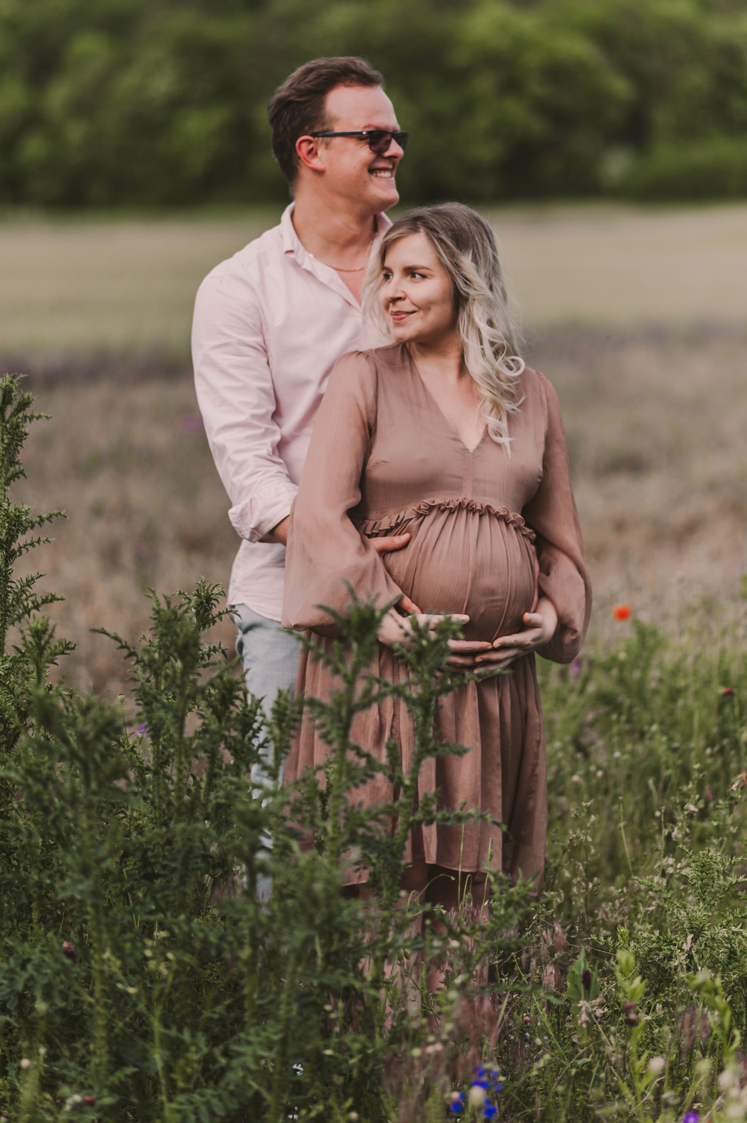 A couple shares an intimate embrace while standing in a field of wild flowers and tall grass.
