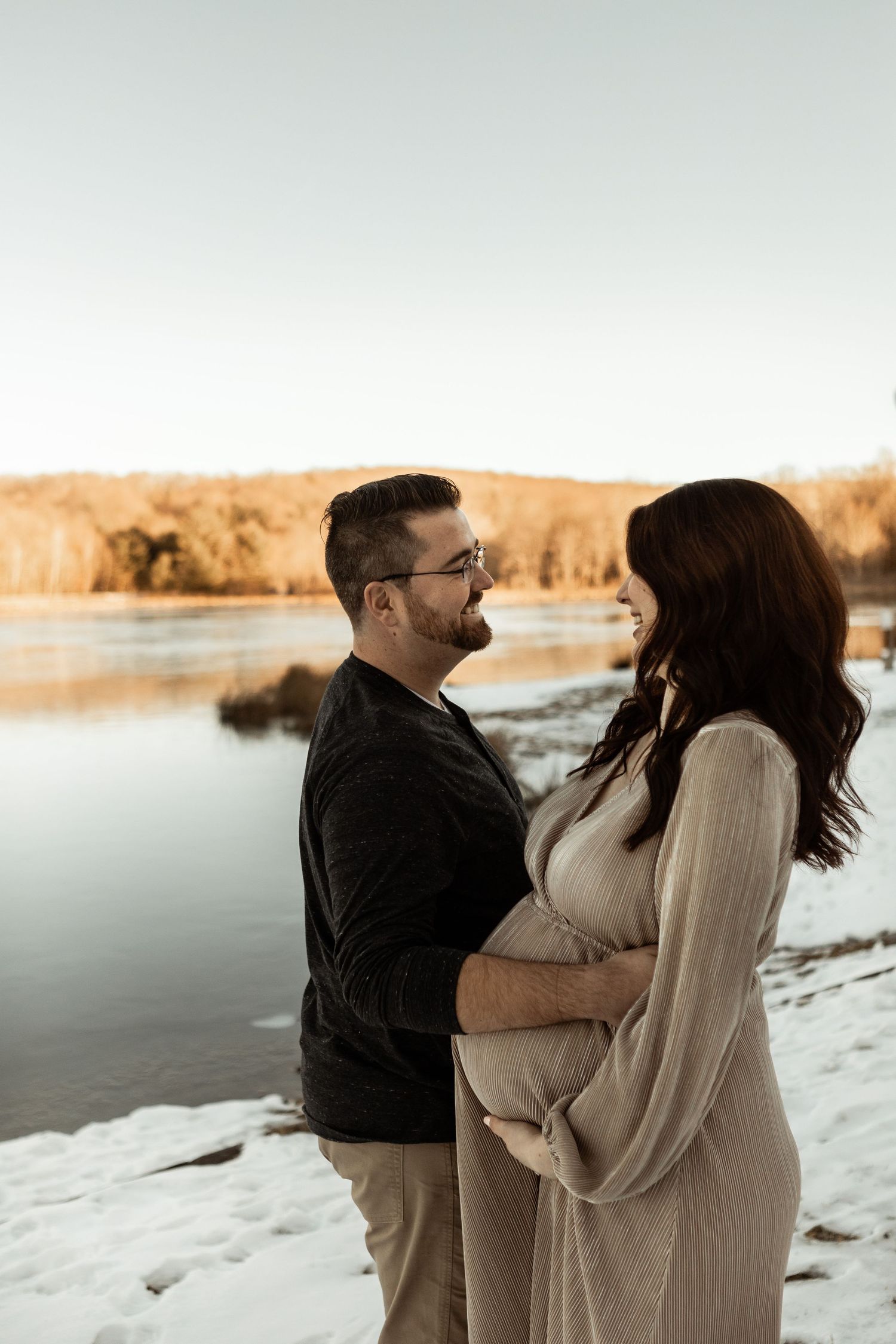 Couple embracing near water during sunset in winter landscape.