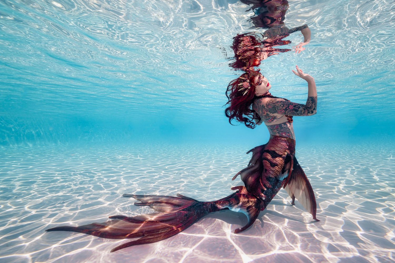 Underwater dancer in flowing dress creates graceful poses in crystal clear pool.