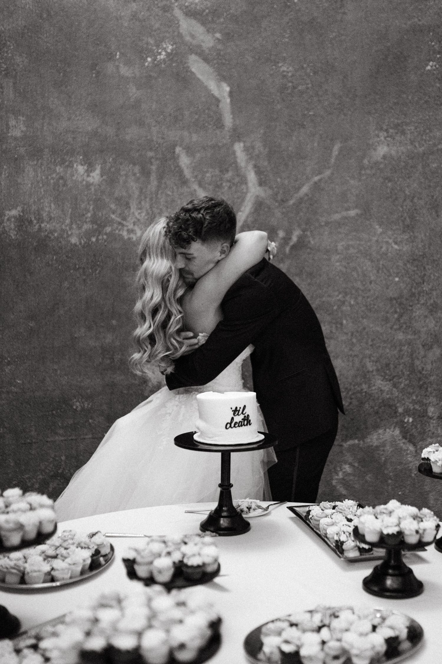 A romantic black and white moment between newlyweds near their wedding cake and dessert display.