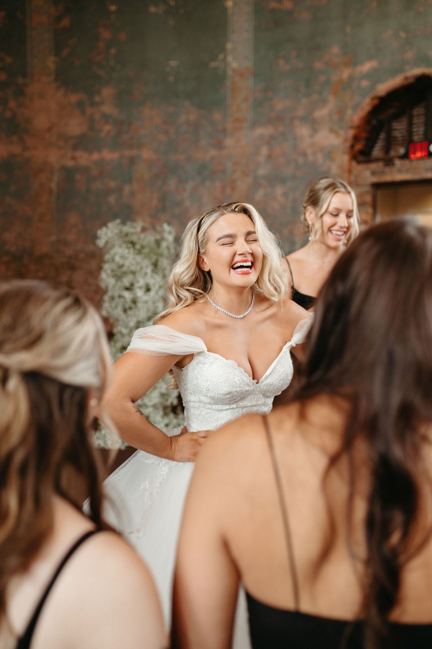A joyful bride in white surrounded by bridesmaids laughs during wedding celebrations.