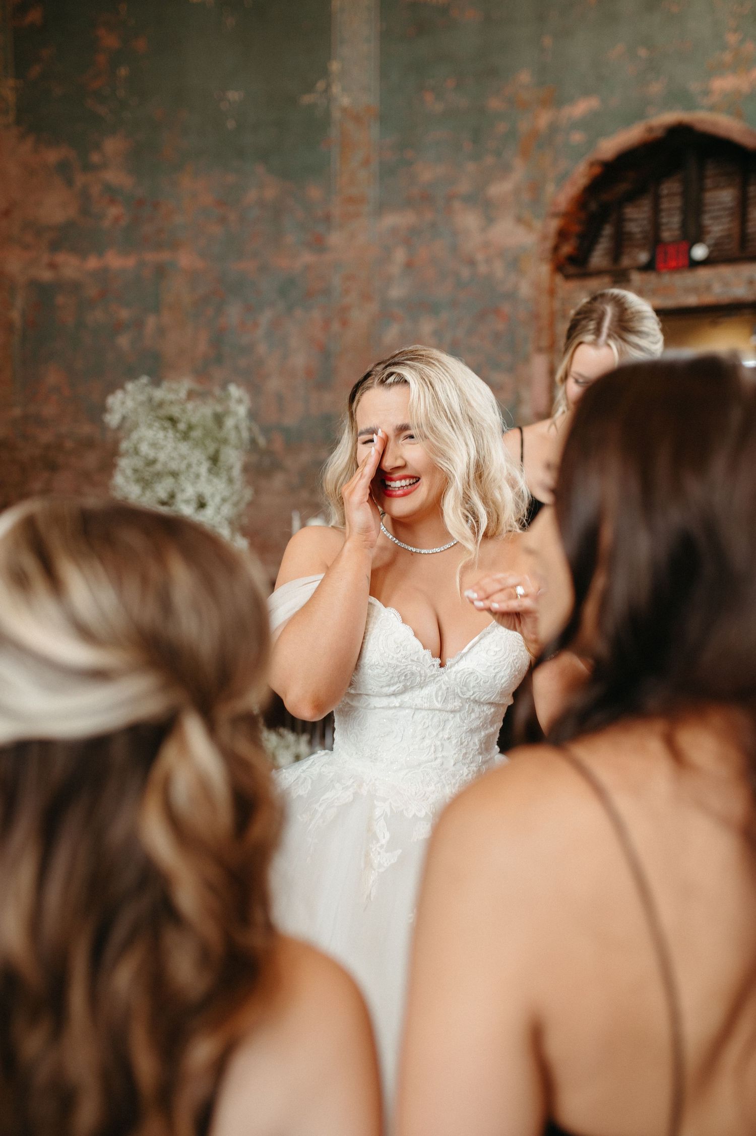 A bride in a white dress shares a candid laughing moment with her wedding party.