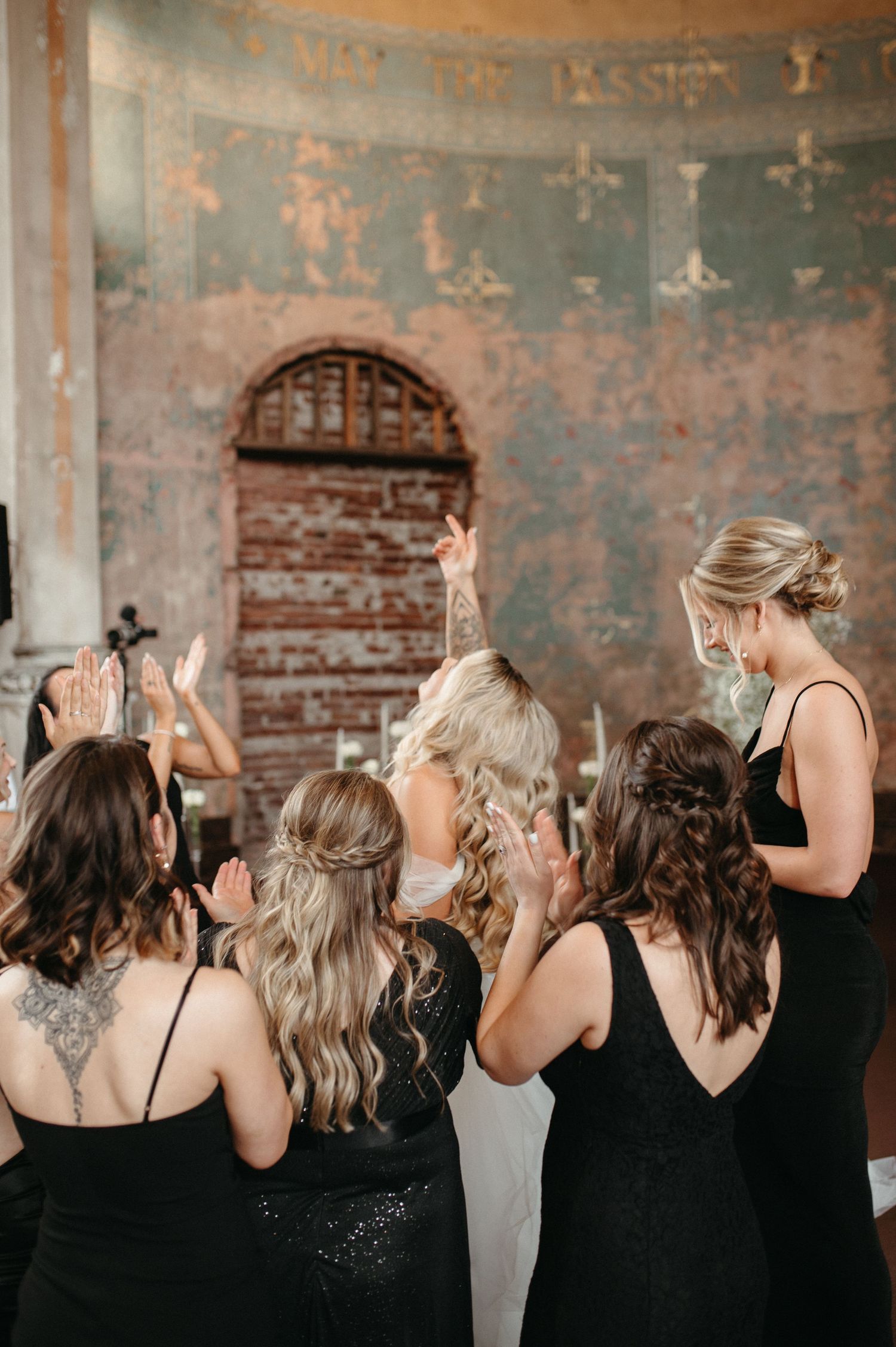 Wedding party raises hands in celebration against distressed painted walls.