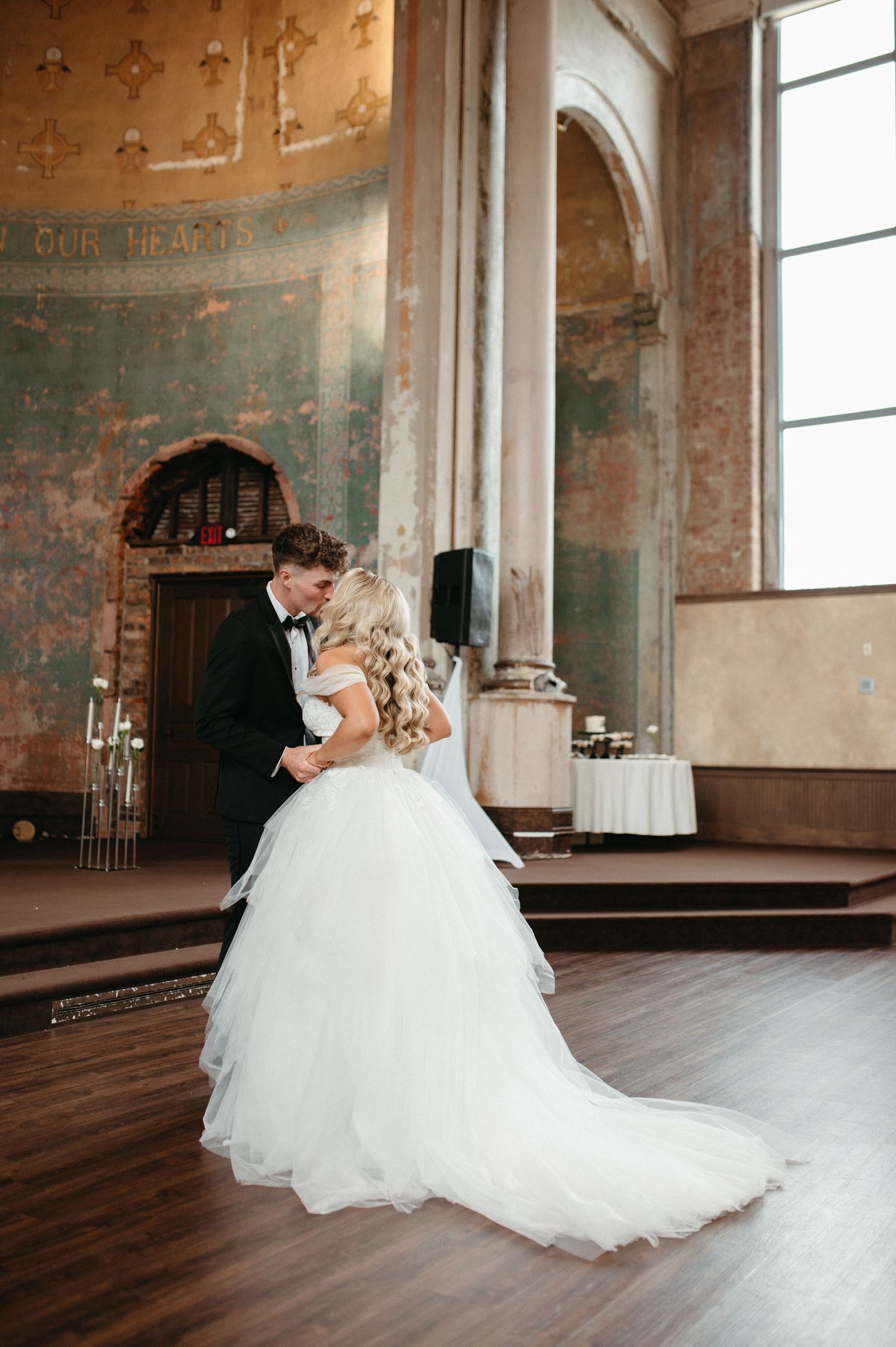 Romantic dance moment in venue with distressed walls and tall windows.