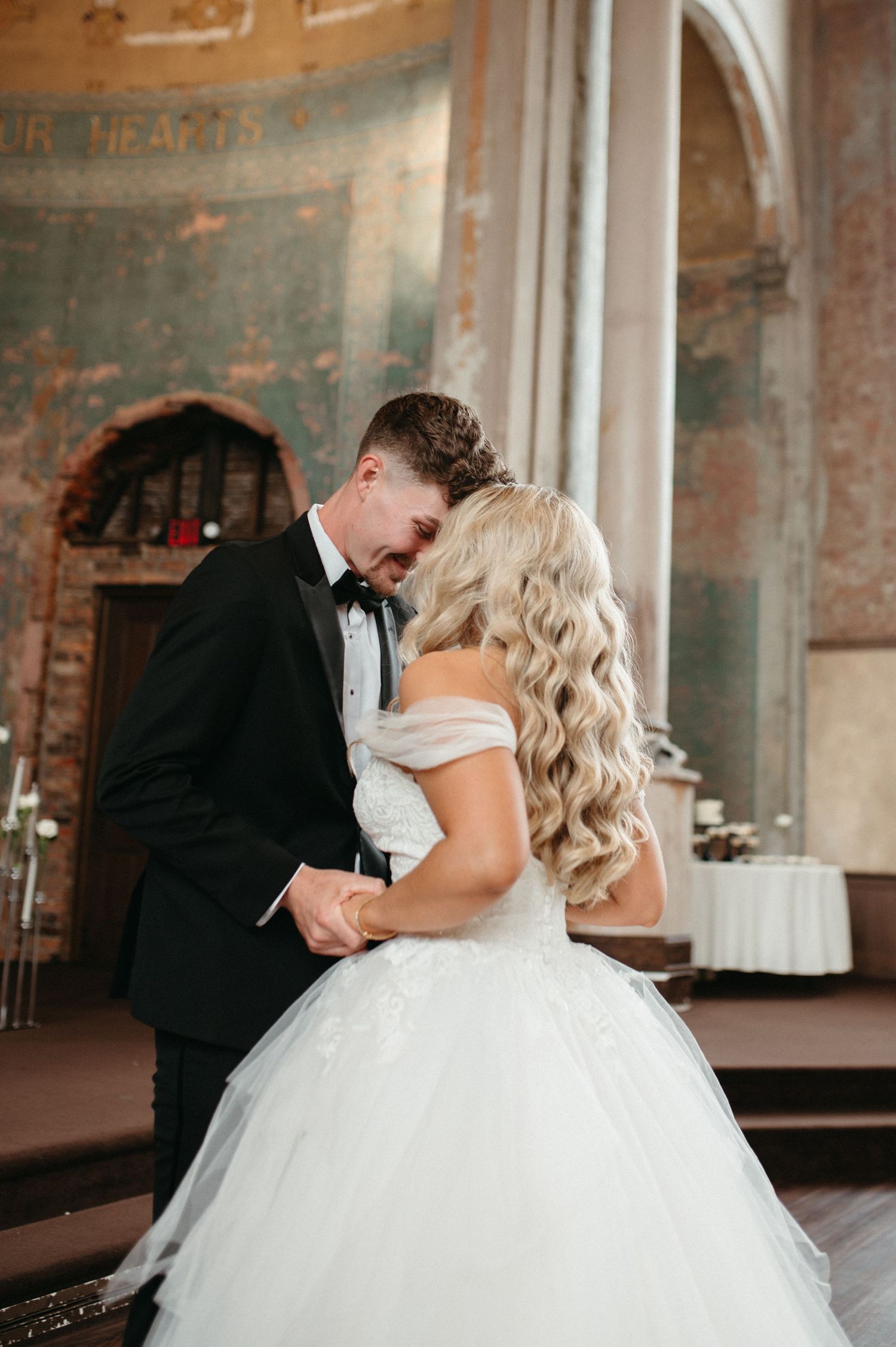 A romantic wedding moment in a historic venue with textured walls as the couple shares a tender dance.
